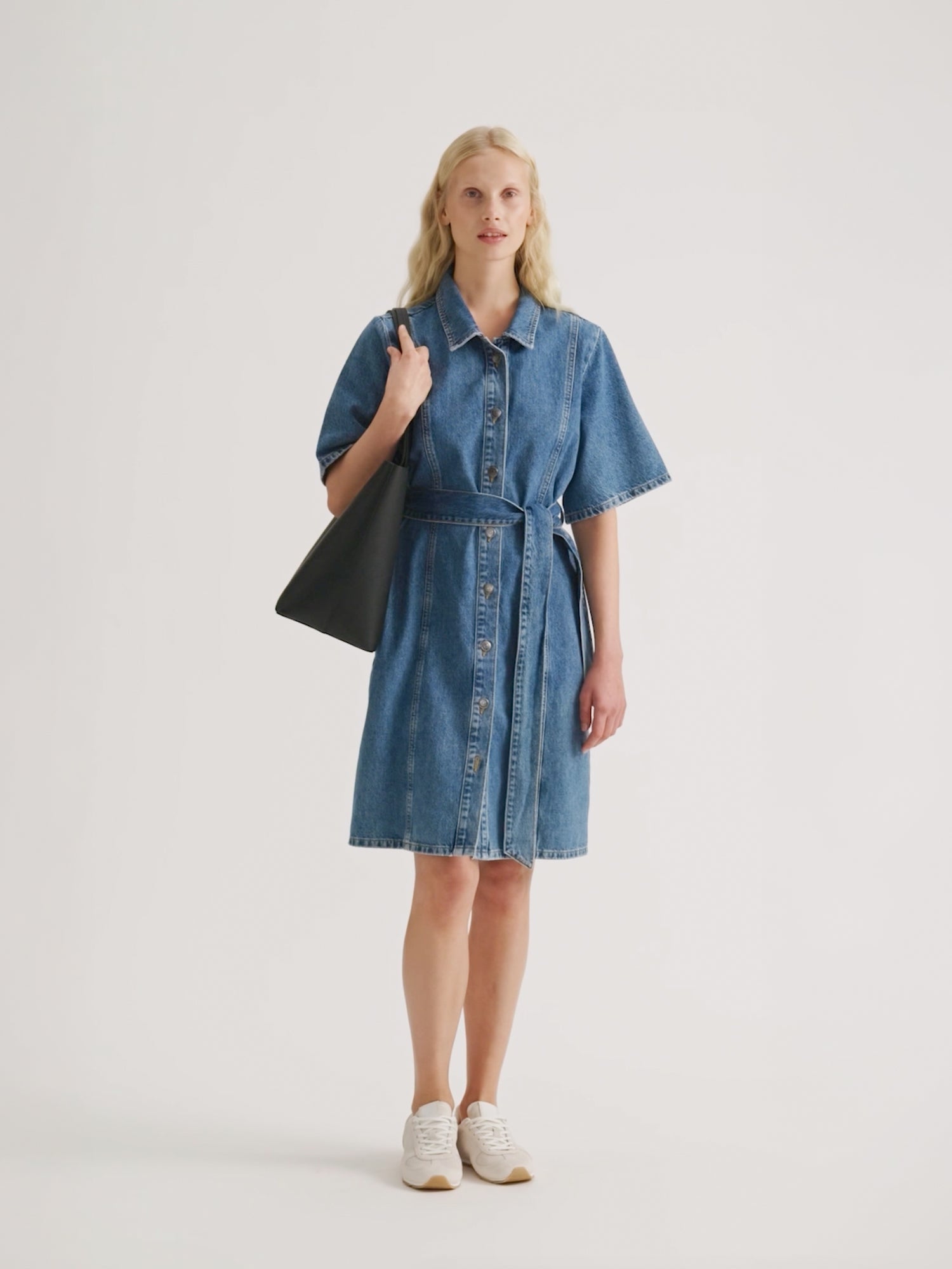 Naisten trendikäs Doris-farkkumekko klassisessa denim -sävyssä mallin yllä tennareiden kanssa.