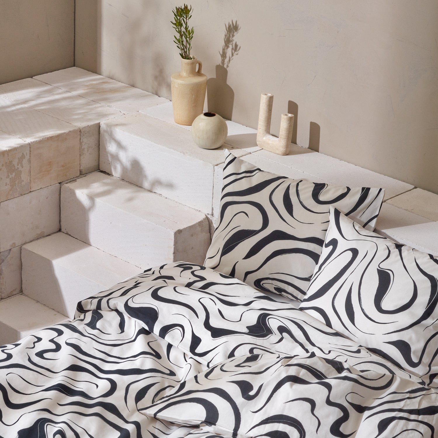 Nanson mustavalkoinen Vesi-pussilakanasetti pedattuna kauniissa asetelmassa maljakkojen kanssa.