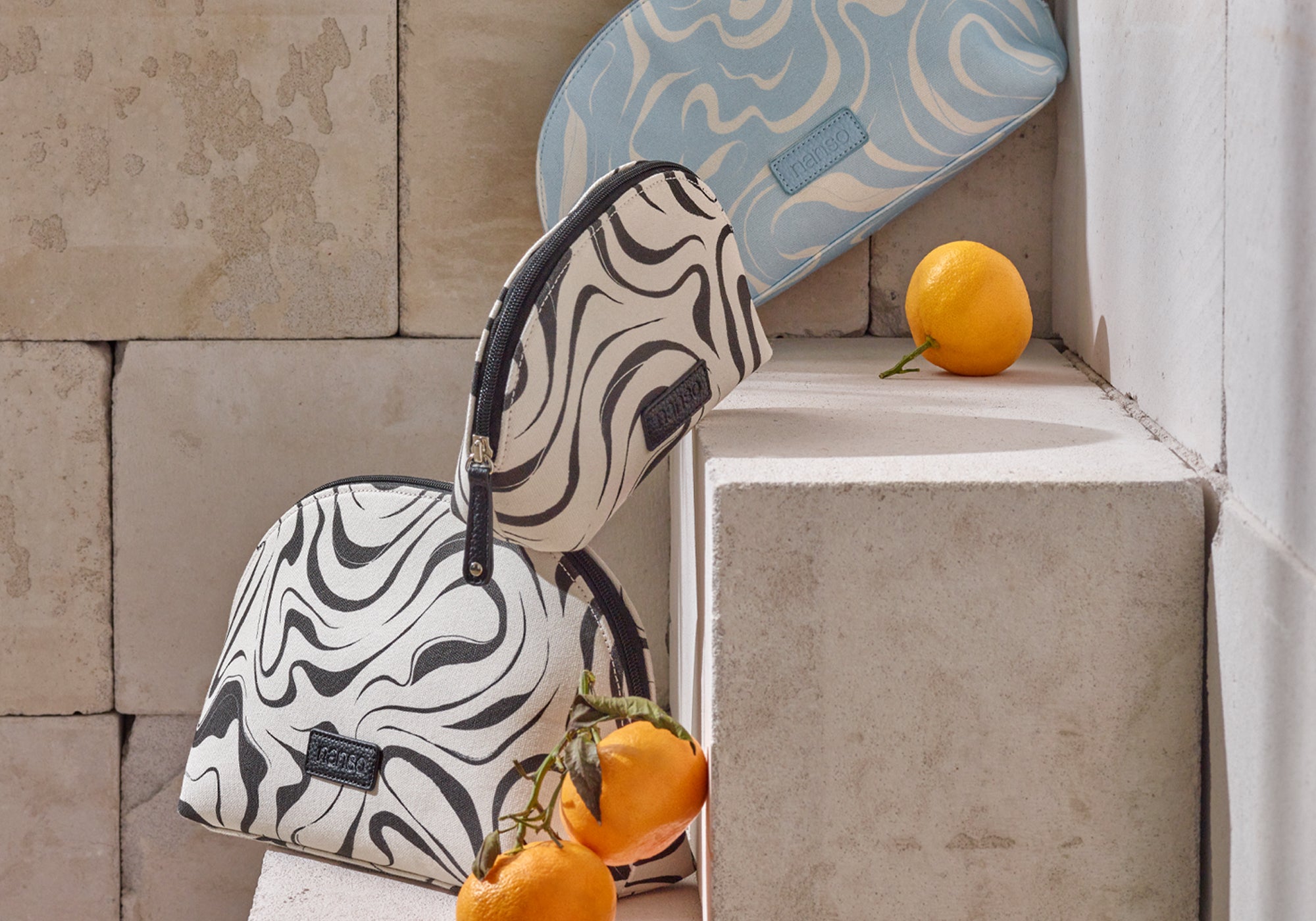 Nanso musta-valkoiset ja vaaleansininen Vesi-kosmetiikkalaukut kuvassa portailla.