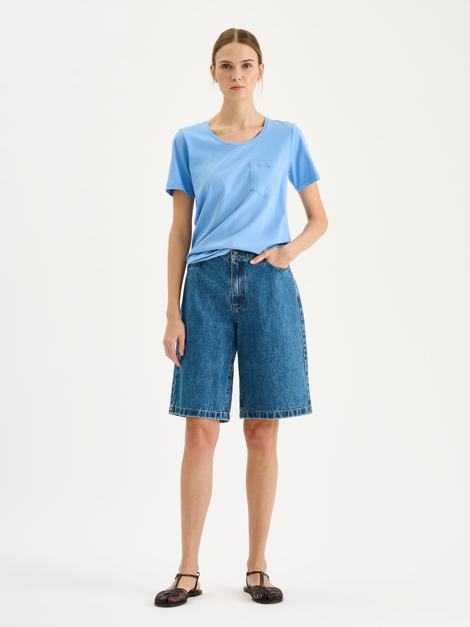 Nanson naisten vaaleansininen Tasku-t-paita pyöreällä pääntiellä mallin päällä farkkushortsien kanssa.