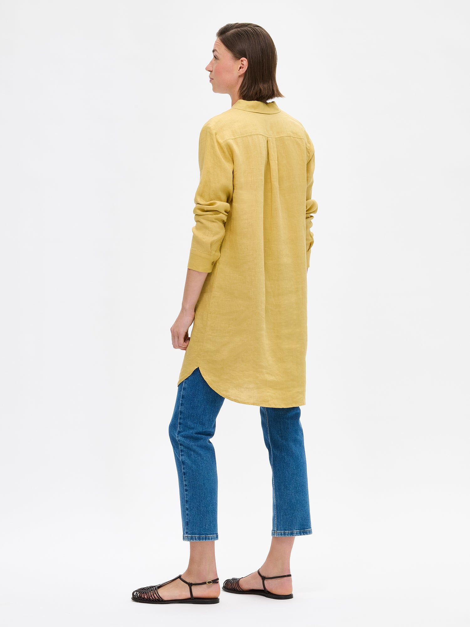 Naisten rento ja pitkä keltainen Pellava-paitapusero mallin päällä sinisten farkkujen ja sandaalien kanssa takaa kuvattuna.