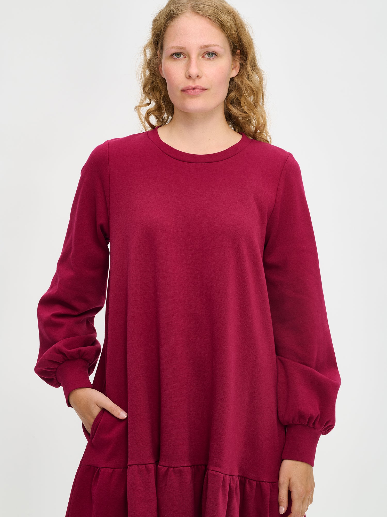 Nanson naisten viininpunainen Leija-mekko mallin yllä lähikuvassa, pyöreä pääntie, pitkät pussihihat ja helman poimutus korostuvat pehmeässä kankaassa.