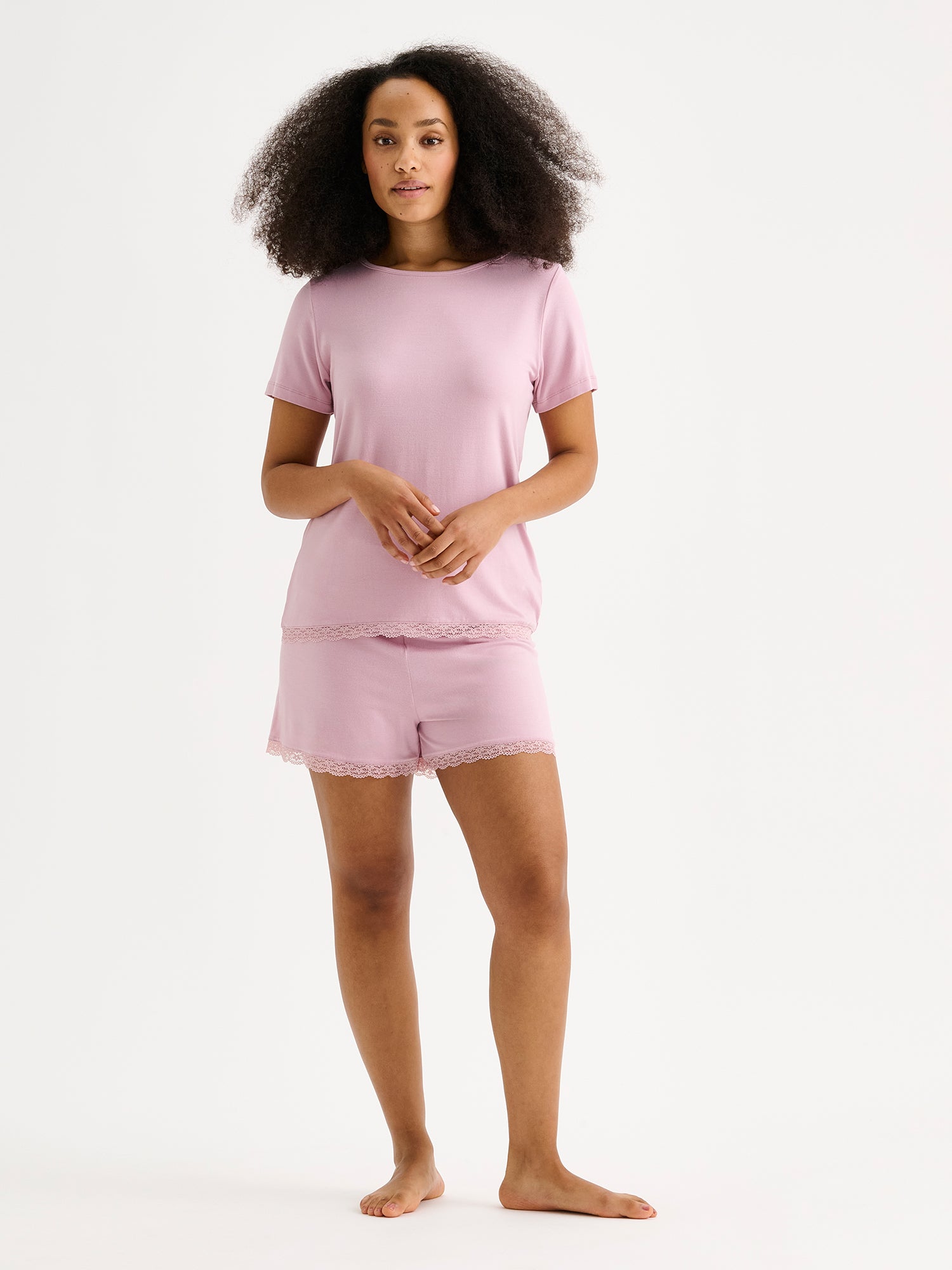 Naisten ylellisen pehmeät vaaleanpunaiset Pitsi-shortsit mukavalla vyötärörakenteella mallin päällä saman sarjan puseron kanssa.