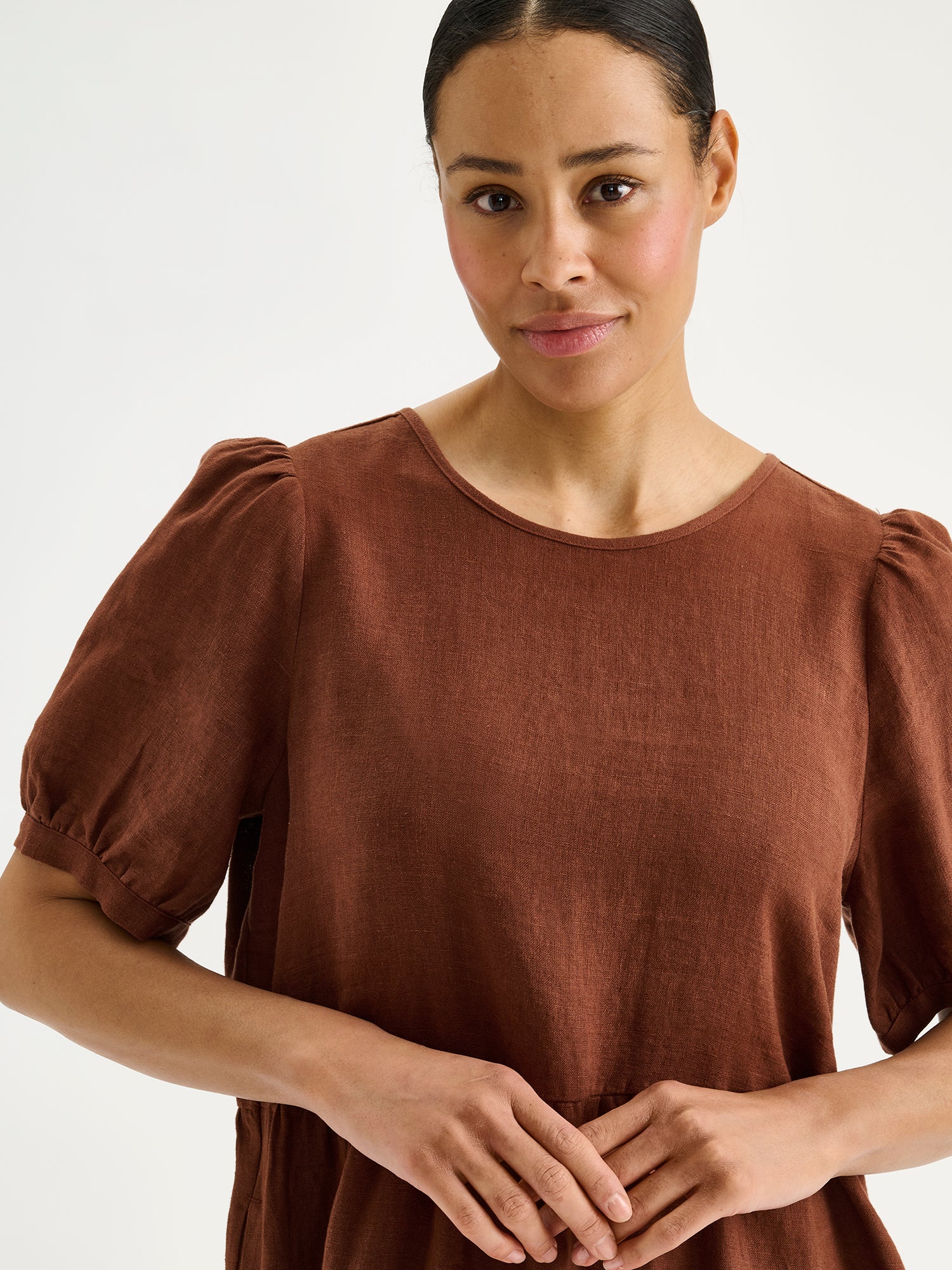 Naisten kaunis ruskea Sarastus-pellavamekko volyymisilla frillakerroksilla ja lyhyillä puhvihihoilla mallin päällä lähikuvassa.