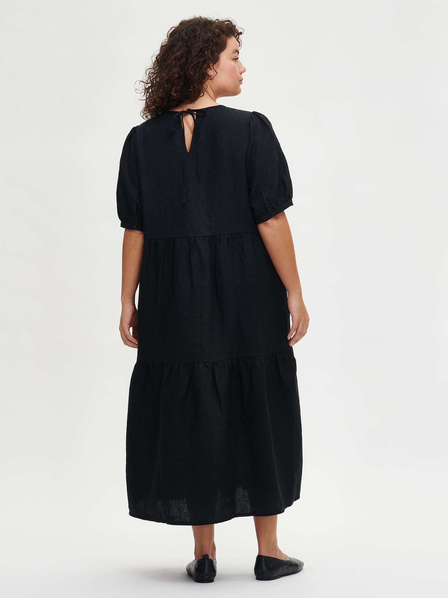 Nanson naisten kaunis musta Sarastus-pellavamekko volyymisilla frillakerroksilla ja lyhyillä puhvihihoilla mallin päällä koossa XL takaa.