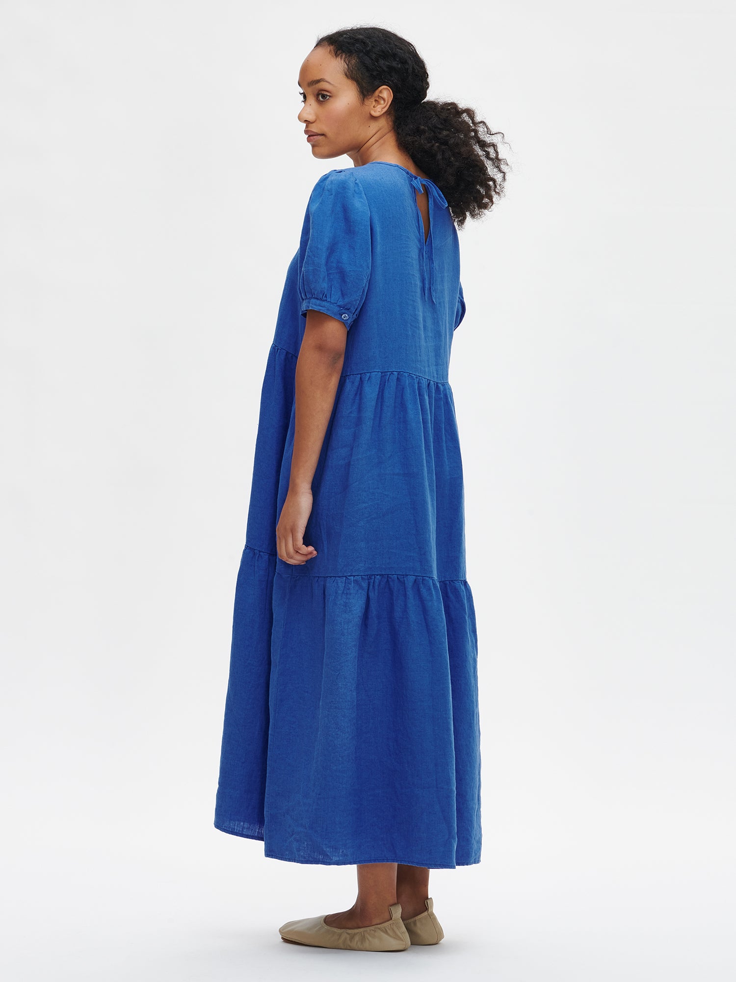 Nanson naisten kaunis sininen Sarastus-pellavamekko volyymisilla frillakerroksilla ja lyhyillä puhvihihoilla mallin päällä takaa.