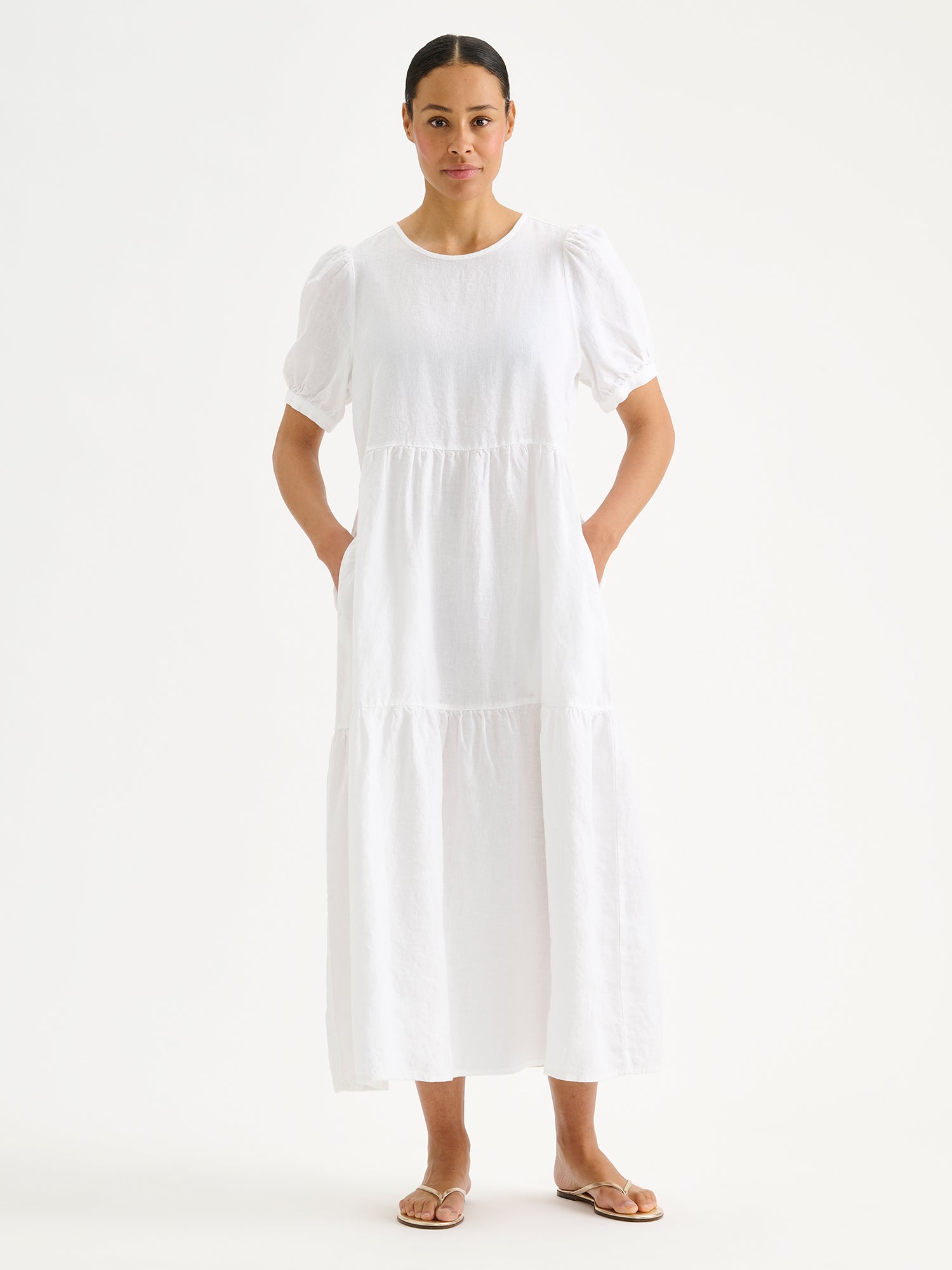 Naisten kaunis valkoinen Sarastus-pellavamekko volyymisilla frillakerroksilla ja lyhyillä puhvihihoilla mallin päällä.