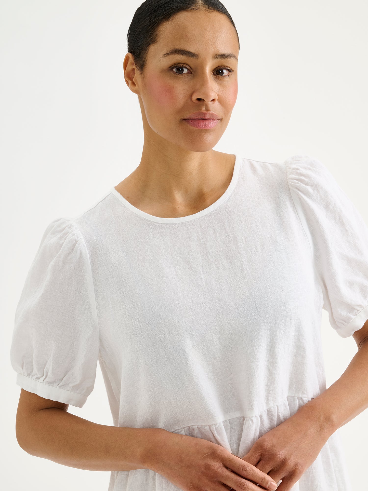 Naisten kaunis valkoinen Sarastus-pellavamekko volyymisilla frillakerroksilla ja lyhyillä puhvihihoilla mallin päällä lähikuvassa.