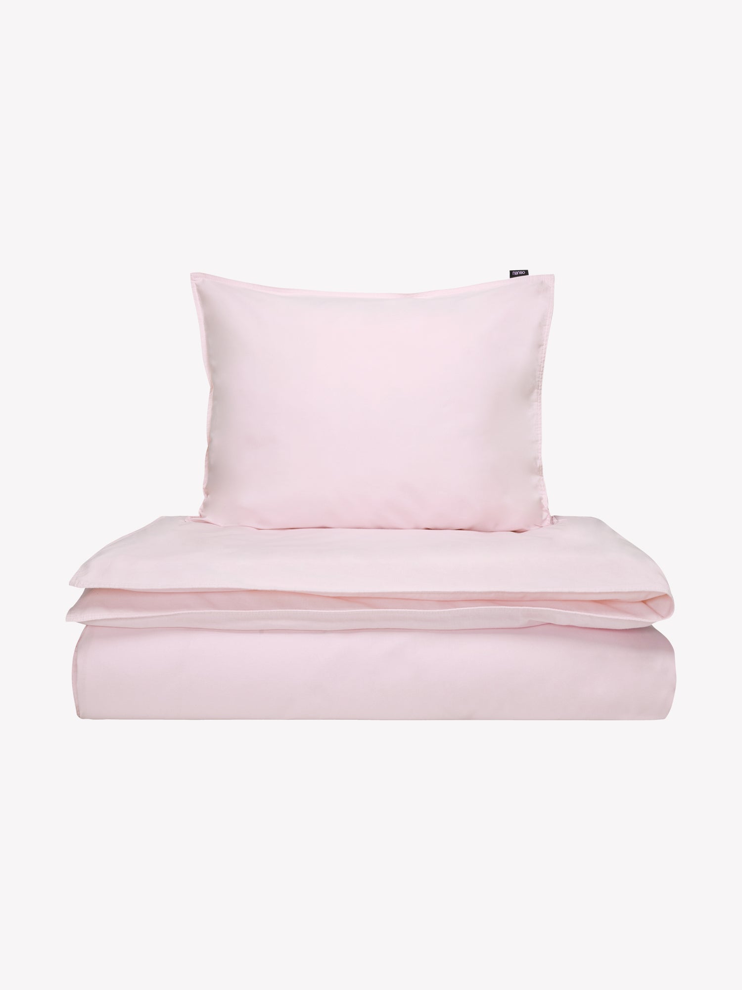 Nanson vaaleanpunainen Uni-pussilakana kivipestystä tiiviistä ja korkealaatuisesta puuvillakankaasta tuotekuvassa täkin ja tyynyn päällä.