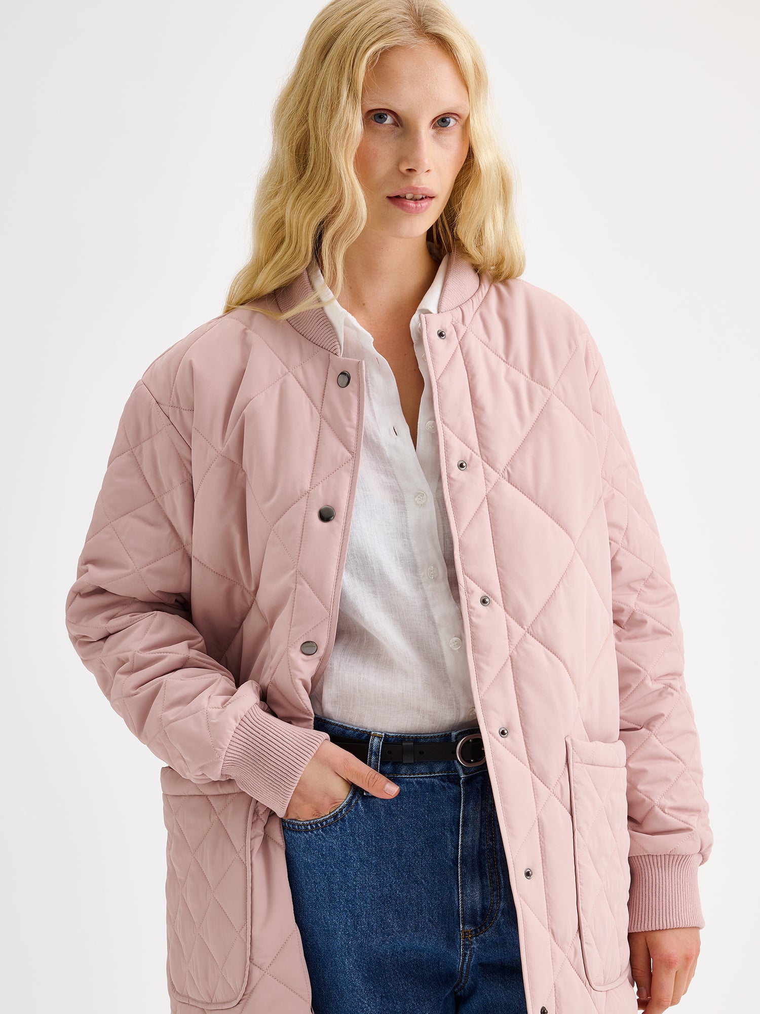 Nanson naisten Midi Tikkitakki pudotetulla olkalinjalla ja kevyellä vanulla. Takin pääntiellä ja hihansuissa on mukava neulosresori ja edessä nepparikiinnitys sekä päällitaskut. Kuvattuna mallin päällä edestä läheltä.