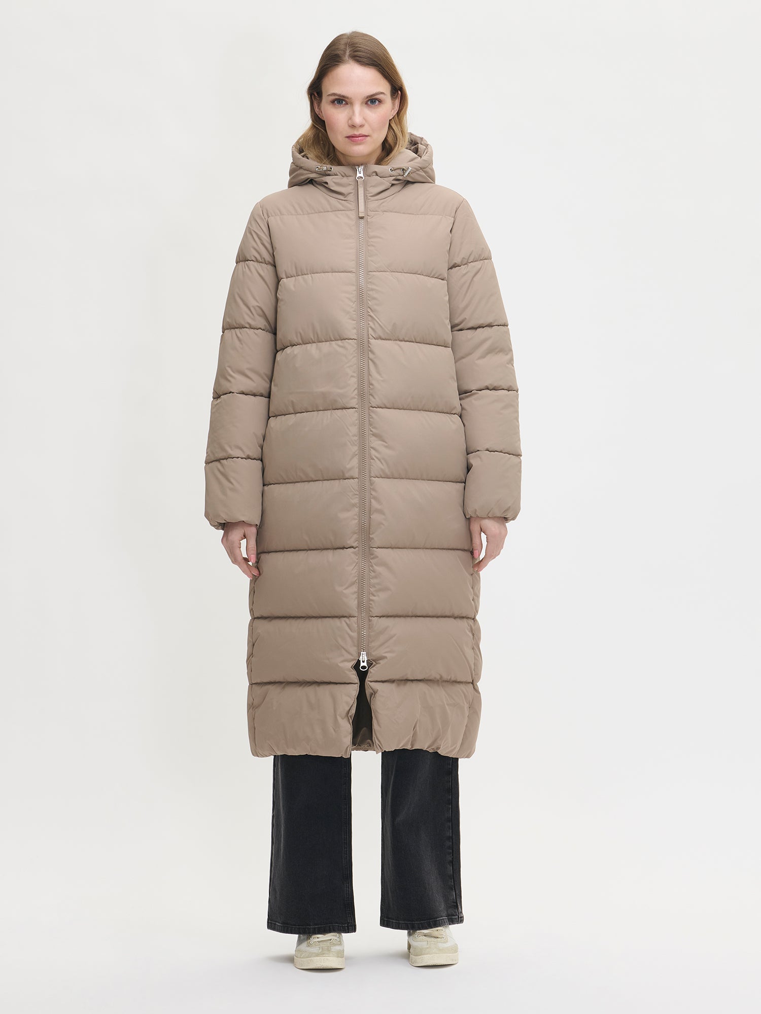 Lämmin ja muhkea pitkä beige Lumi-toppatakki miellyttävän kevyellä vanuvuorella. Mallin päällä edestä.