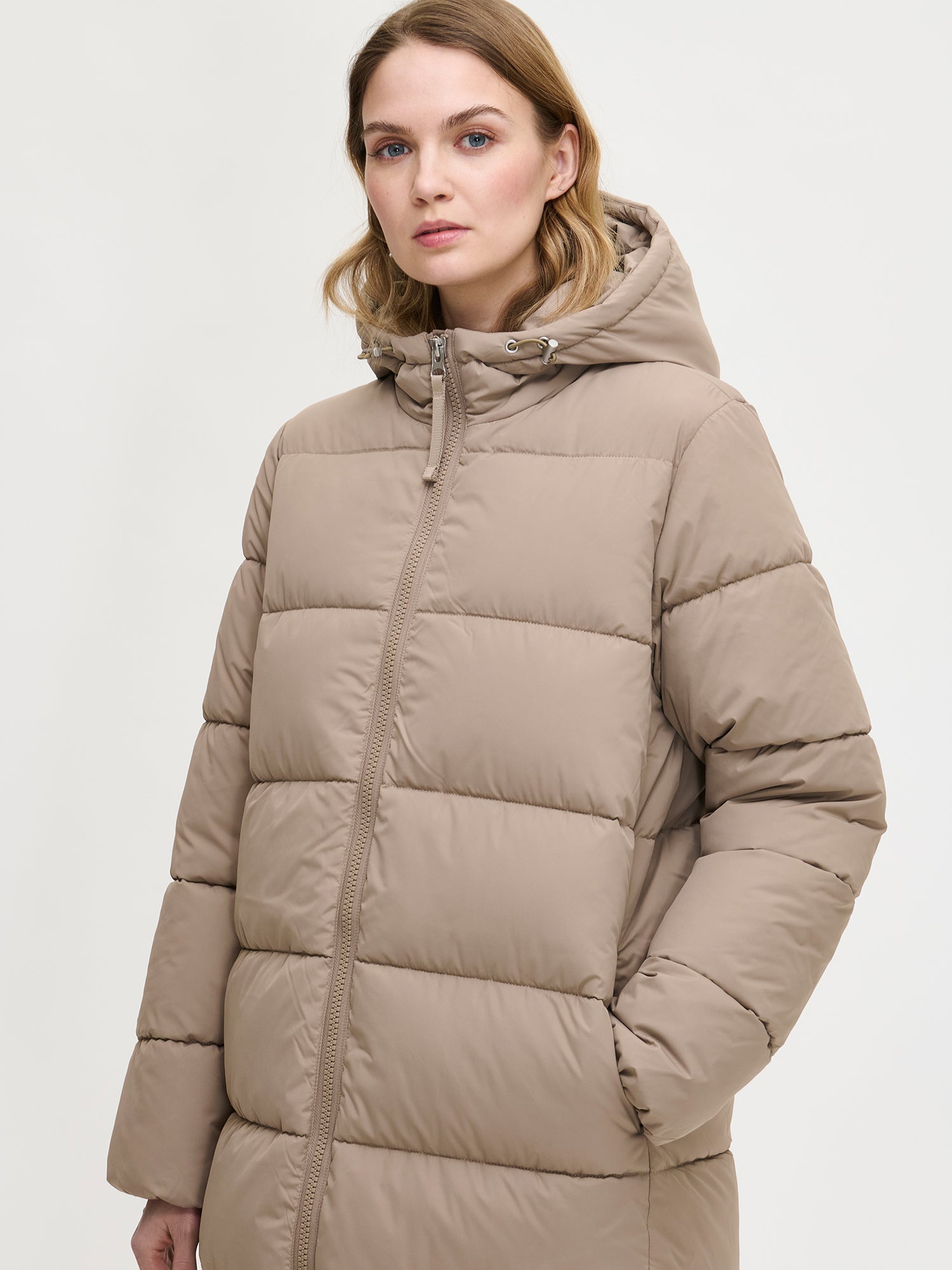 Lämmin ja muhkea pitkä beige Lumi-toppatakki miellyttävän kevyellä vanuvuorella. Mallin päällä edestä läheltä.