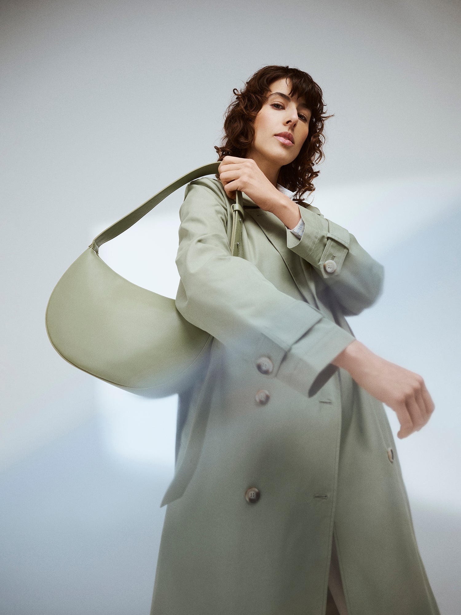 Nanson naisten klassisen tyylikäs vaaleanvihreä Trenssi-takki tummahiuksisen mallin päällä Olka Kuu -laukun kanssa.