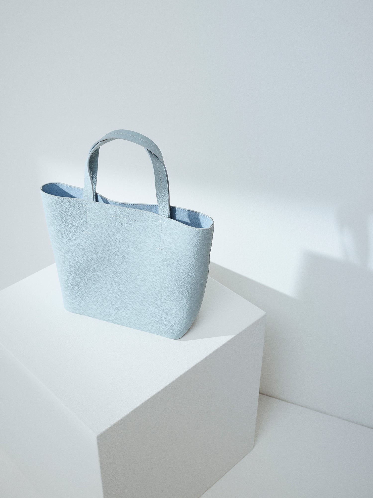 Nanson tyylikäs vaaleansininen Naru Tote- nahkalaukku. Naru Tote -nahkalaukussa on sekä lyhyemmät kantohihnat että pidempi irrotettava ja säädettävä olkahihna. Tuote on valmistettu sertifioidusta nahasta. Brändikuva edestä ilman hihnaa.