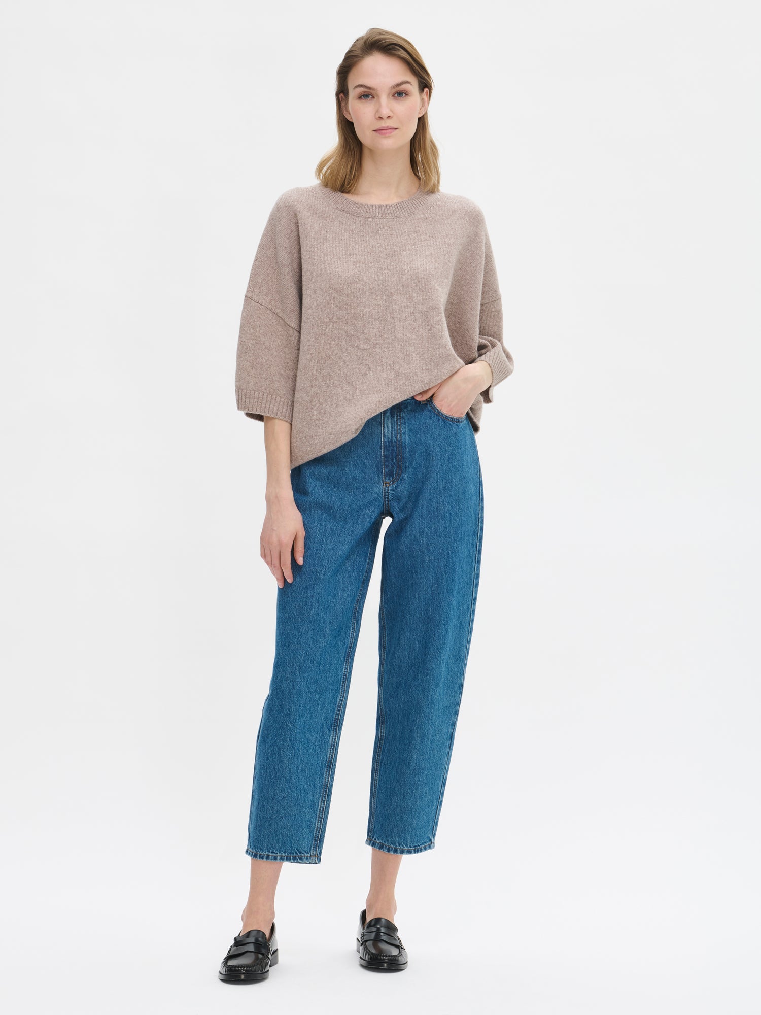 Naisten rento Oversize-tyylinen harmaanbeige Lana-neulepaita, jossa pyöreä resoripääntie, 1/2 pituiset hihat ja ribbineulos hihansuissa ja helmassa. Kuvassa mallin päällä farkkujen kanssa.