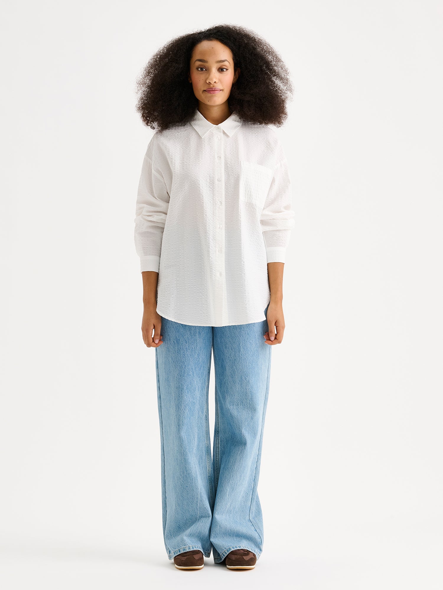 Nanson naisten tyylikäs sininen Maari-paitapusero, jossa kaulus, pudotettu olkalinja, rintatasku ja napit edessä. Kevyessä kudotussa materiaalissa on kaunis pintastruktuuri. Kuvassa mallin päällä farkkujen kanssa.