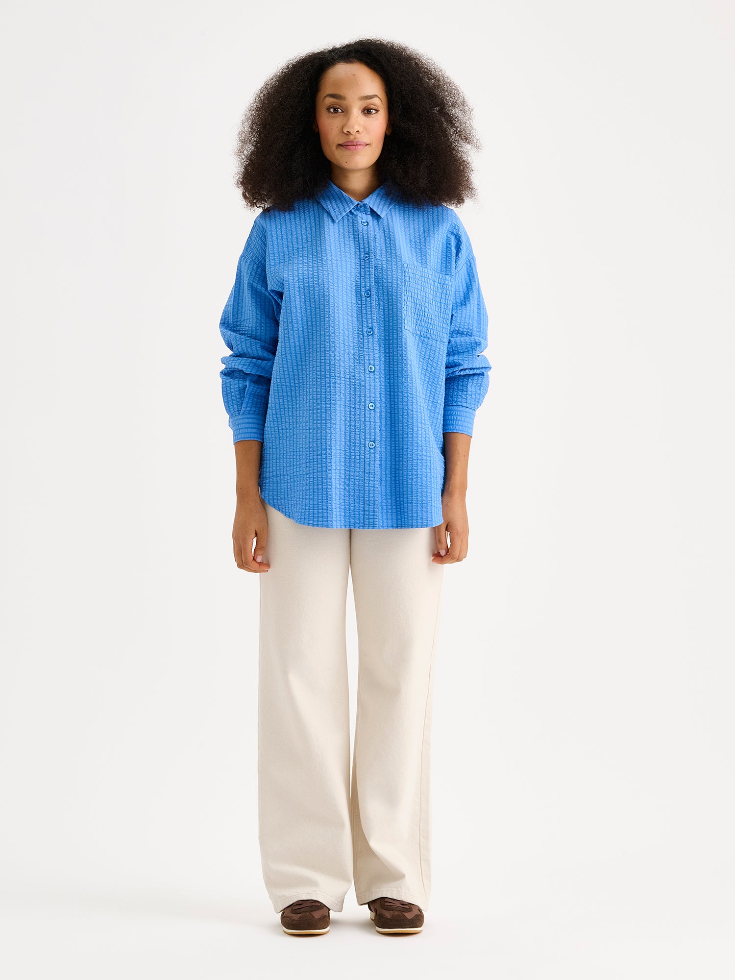 Nanson naisten tyylikäs sininen Maari-paitapusero, jossa kaulus, pudotettu olkalinja, rintatasku ja napit edessä. Kevyessä kudotussa materiaalissa on kaunis pintastruktuuri. Kuvassa mallin päällä vaaleiden farkkujen kanssa.