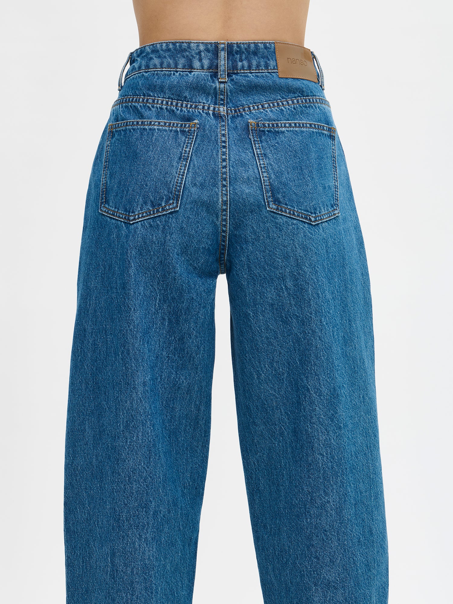 Nanson naisten barrel leg- tyyliset väljät siniset Rento-farkut. Farkuissa on normaalikorkuinen vyötärö, edessä vetoketju ja nappikiinnitys. Lahkeet ovat väljät ja kapenevat hieman kohti lahkeensuuta. Mallin päällä läheltä takaa kuvattuna.