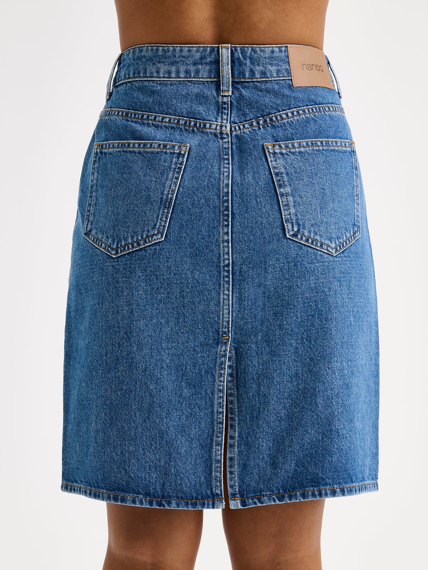 Naisten yhtäaikaa trendikäs ja ajaton Doris-denimhame on monikäyttöinen vaatekaapin peruspilari, joka on helppo yhdistää monenlaisien yläosien kanssa. Lähikuva takaa mallin päällä.