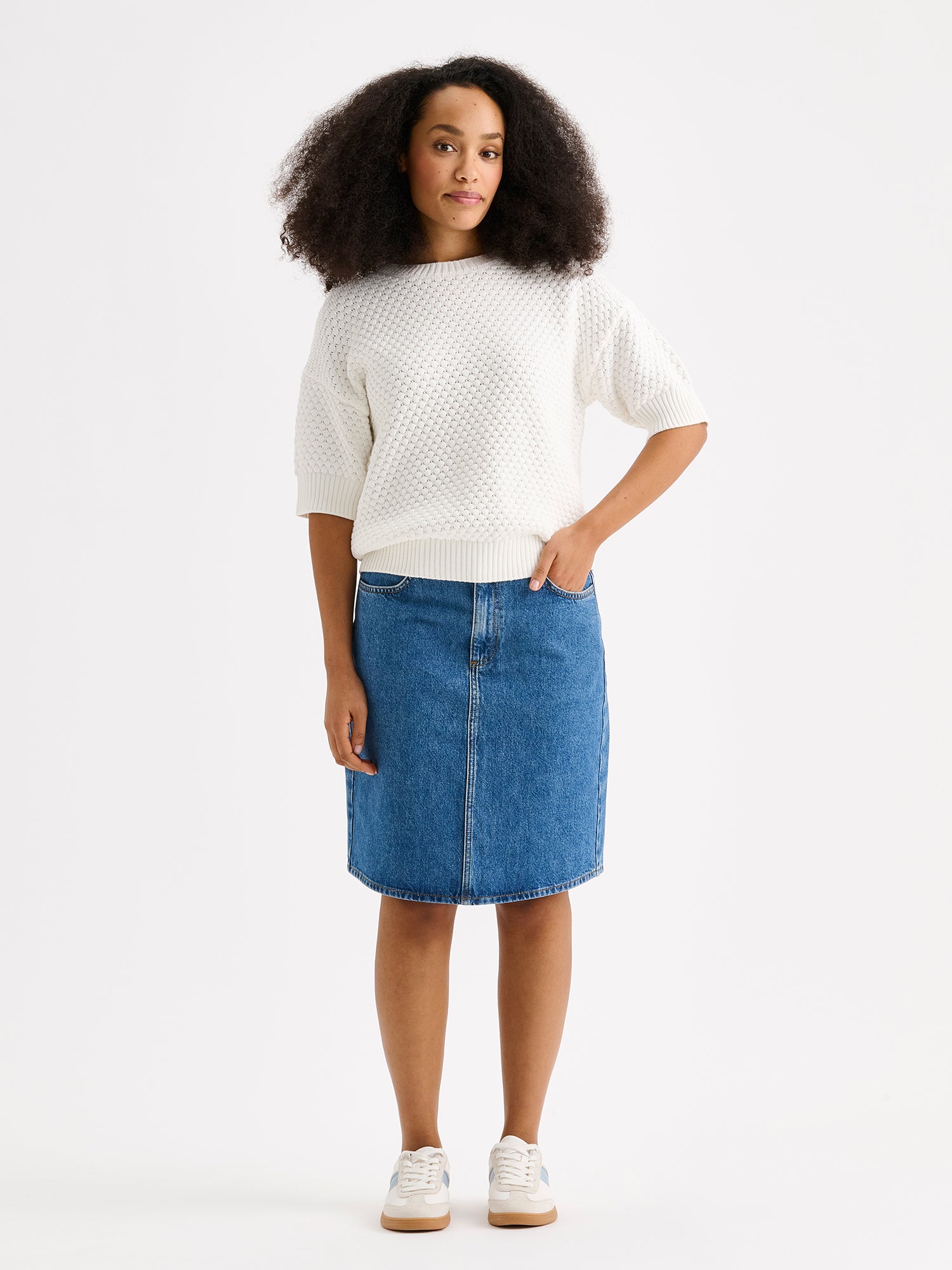 Naisten yhtäaikaa trendikäs ja ajaton Doris-denimhame on monikäyttöinen vaatekaapin peruspilari, joka on helppo yhdistää monenlaisien yläosien kanssa. Kuvassa mallin päällä valkoisen neulepaidan kanssa.