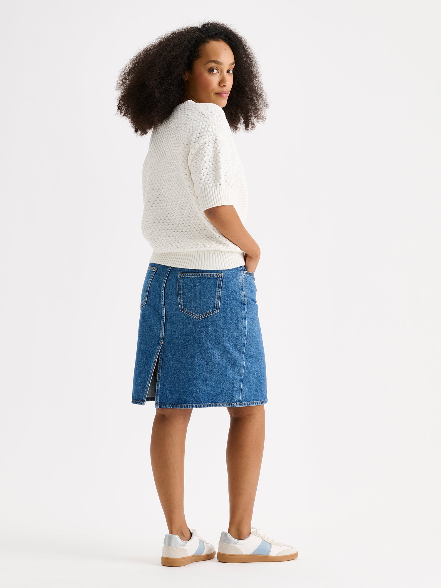 Naisten yhtäaikaa trendikäs ja ajaton Doris-denimhame on monikäyttöinen vaatekaapin peruspilari, joka on helppo yhdistää monenlaisien yläosien kanssa. Kuvassa mallin päällä valkoisen neulepaidan kanssa takaa kuvattuna.