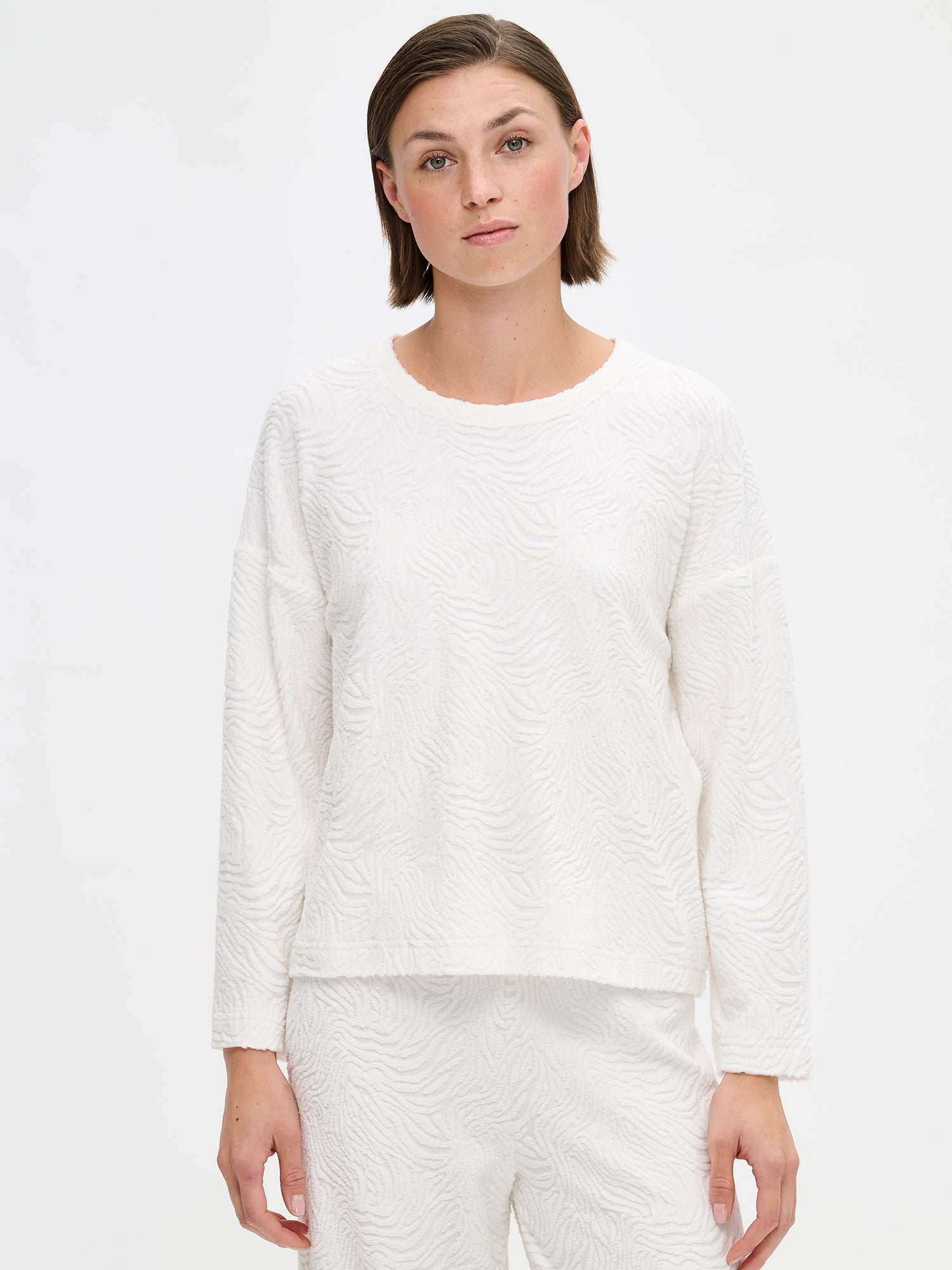 Nanson naisten luonnonvalkoinen Väre-paita pitkillä hihoilla ja pyöreällä pääntiellä. Valmistettu mukavasta ja pintakuvioidusta materiaalista. Kuvattuna mallin päällä edestä päin läheltä.