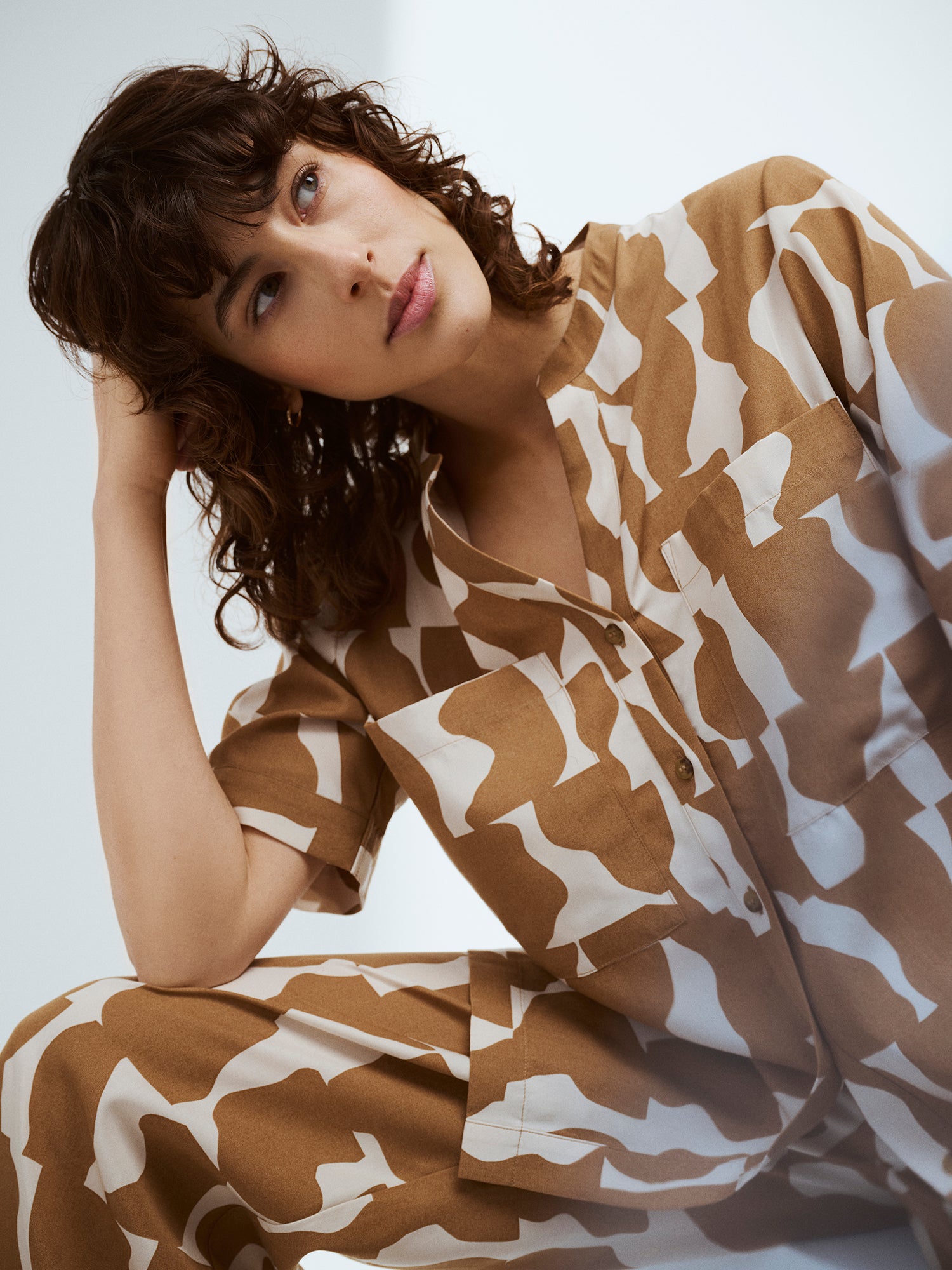 Naisten ihanan rento ja tyylikäs kuosillinen Soraja-pusero ja -housut mallin yllä, malli istuu ja nojaa käteensä rennosti.