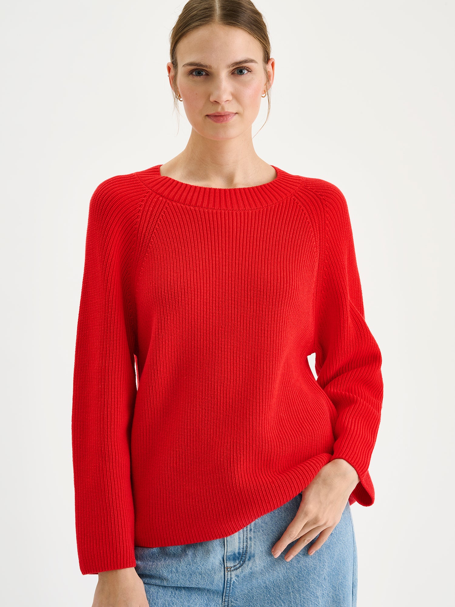 Naisten tyylikäs punainen Kaveri-neulepaita mallin päällä vaaleansinisten farkkujen kanssa lähikuvassa.