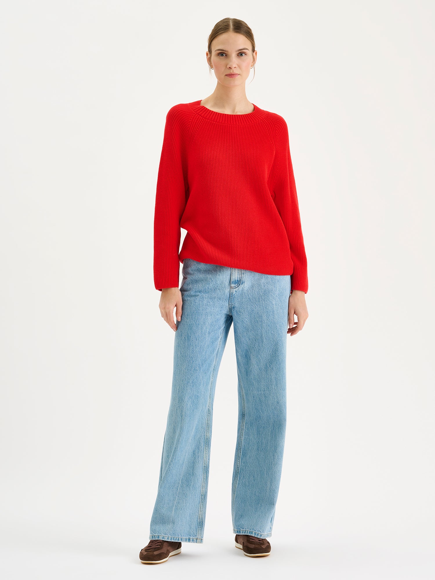 Naisten tyylikäs punainen Kaveri-neulepaita mallin päällä vaaleansinisten farkkujen kanssa.