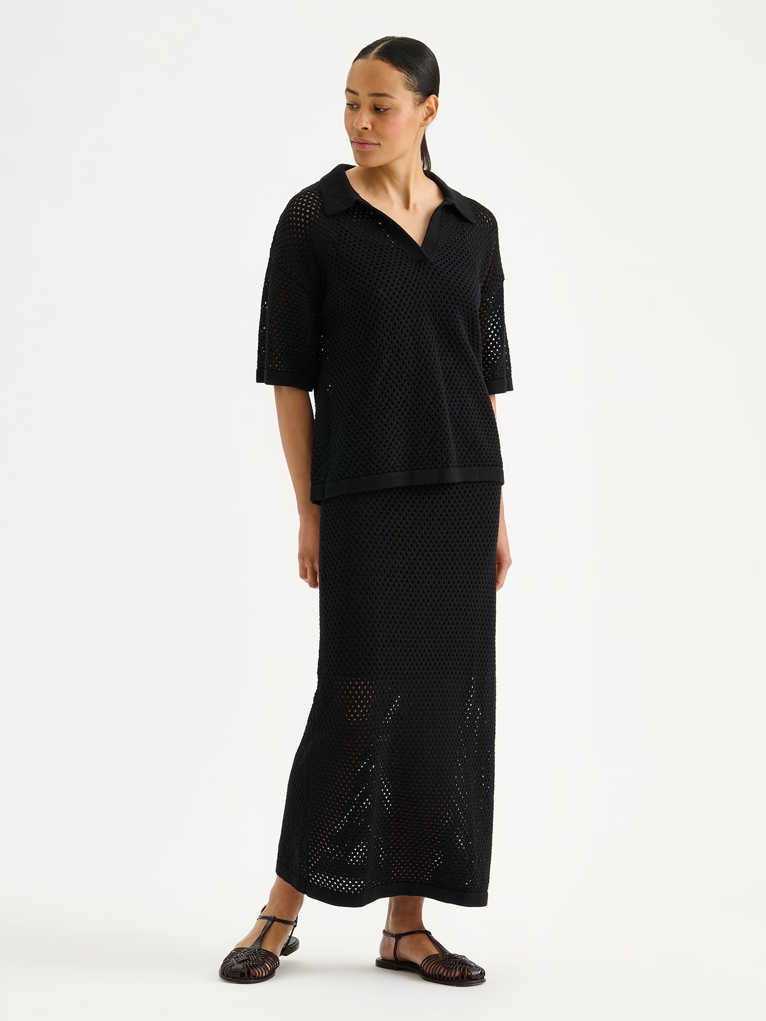 Nanson naisten musta Aure -reikäneulepusero ja -hame mallin päällä sandaalien kanssa.