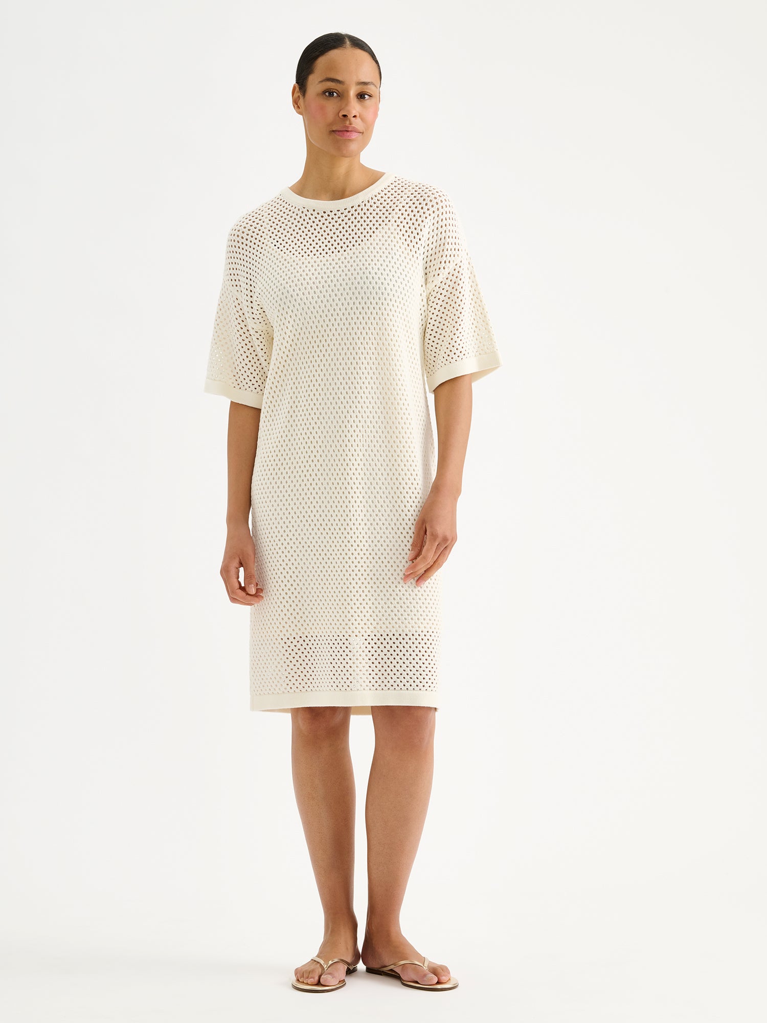 Nanson naisten trendikäs luonnonvalkoinen Aure -reikäneulemekko mallin päällä sandaalien kanssa.