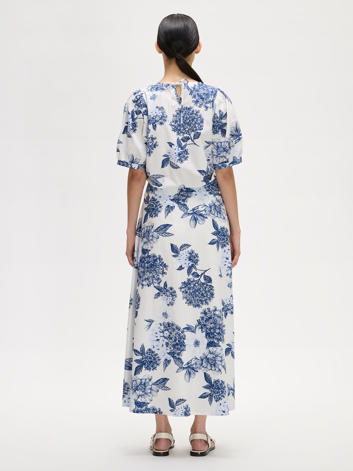 Naisten kuosillinen sini-valkoinen Palatsi-pusero herkällä kukkakuosilla mallin päällä Palatsi-hameen kanssa kuvattuna takaa.