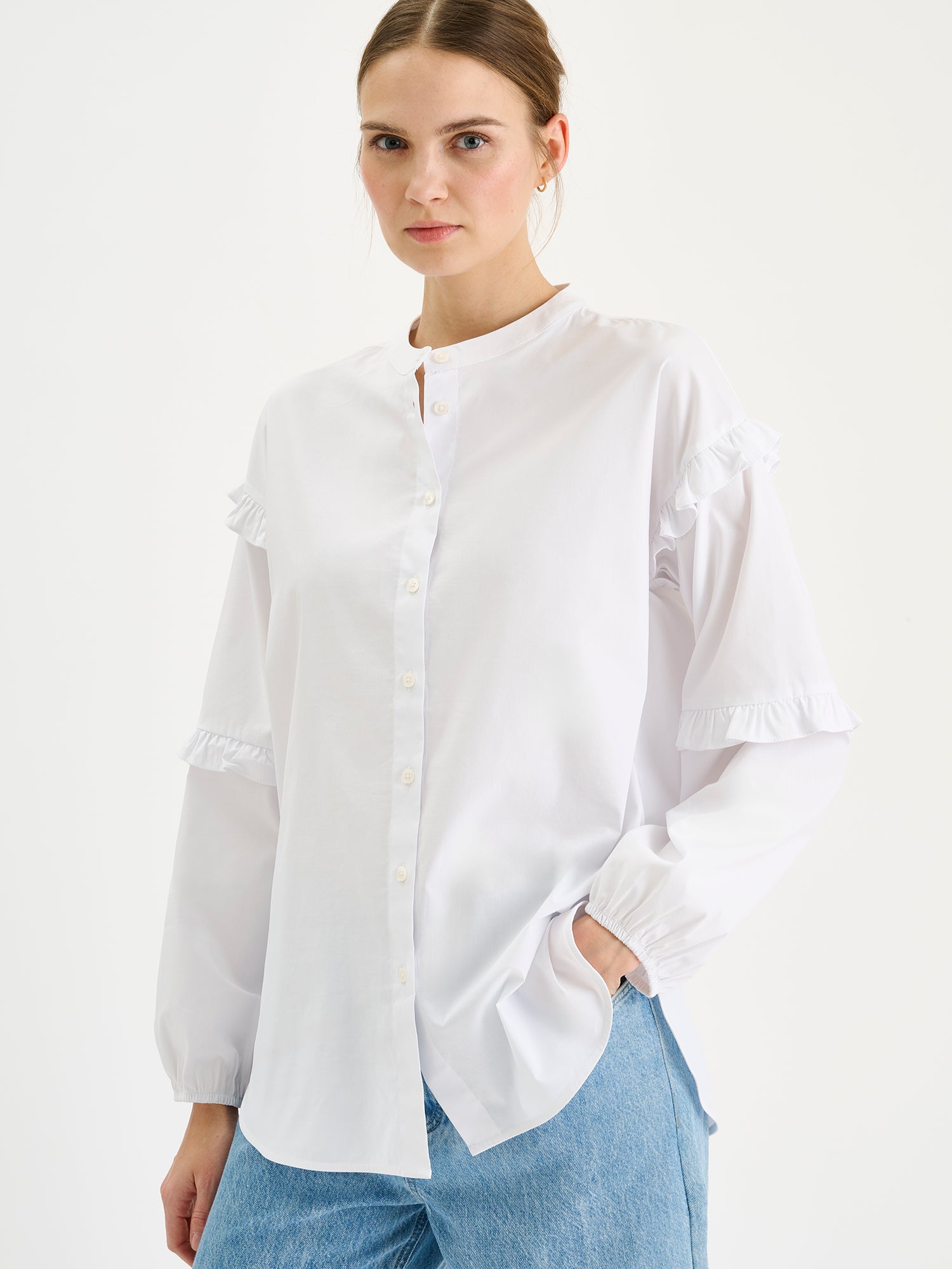 Naisten raikas valkoinen Katri-paitapusero, jossa on kauniit frillayksityiskohdat hihoissa. Lähikuvassa mallin päällä farkkujen kanssa.