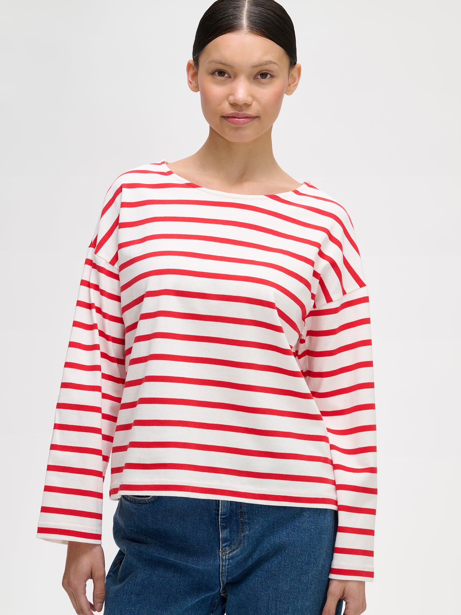 Naisten puna-valko-raidallinen ja ihanan rennon mallinen Breton-pusero mallin päällä farkkujen kanssa lähikuvassa.