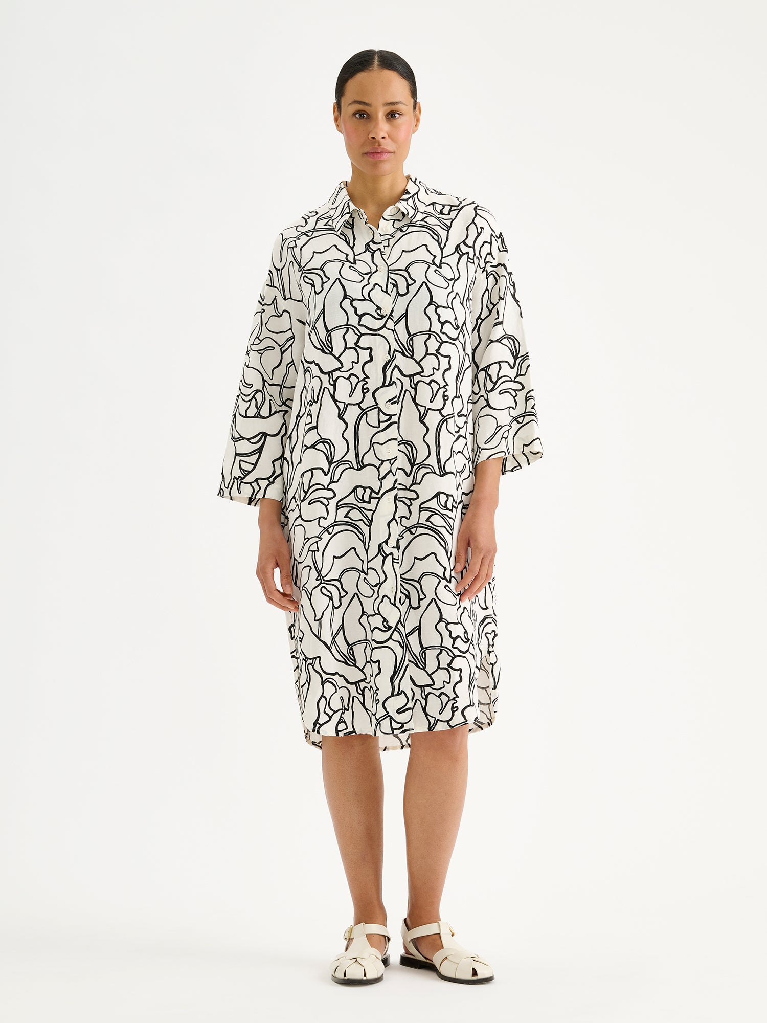 Naisten mukavan rento Iiris-paitamekko, jossa on tyylikäs ja näyttävä mustavalkoinen kukkakuosi mallin päällä sandaalien kanssa.