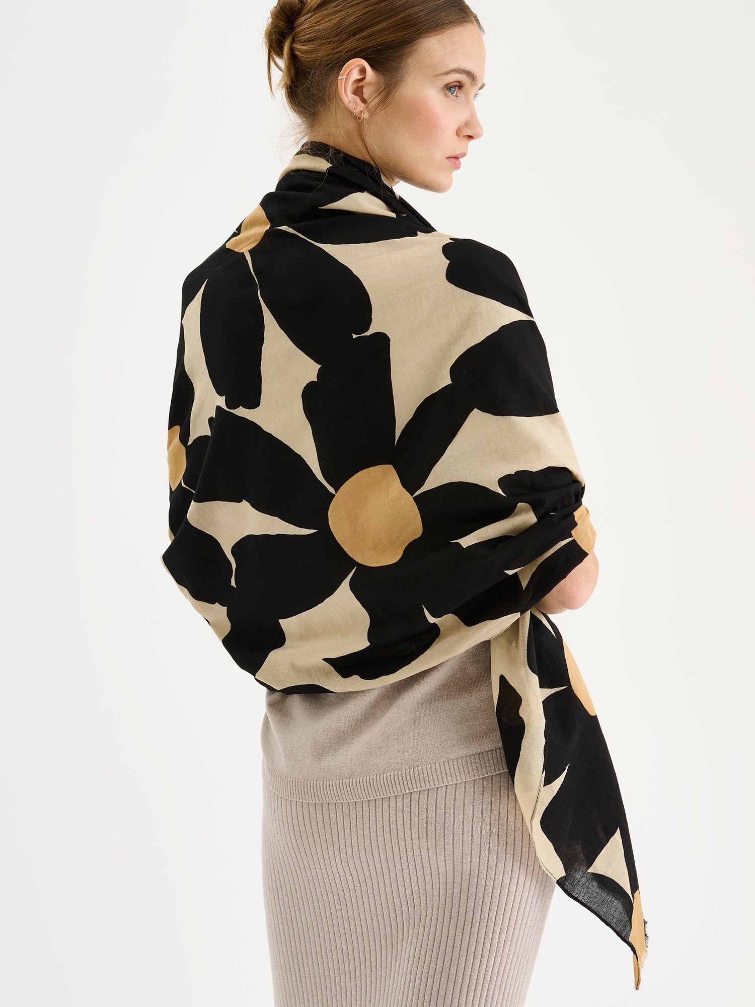 Naisten beige-musta puuvillainen Rosi-huivi näyttävällä ja tyylikkäällä kukkakuviolla mallin hartioilla beigen neulepuseron ja -hameen kanssa.