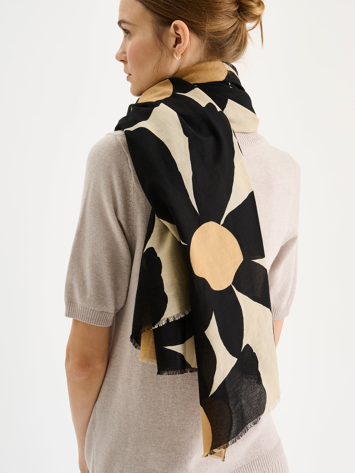 Naisten beige-musta puuvillainen Rosi-huivi näyttävällä ja tyylikkäällä kukkakuviolla mallin kaulassa beigen neulepuseron kanssa.