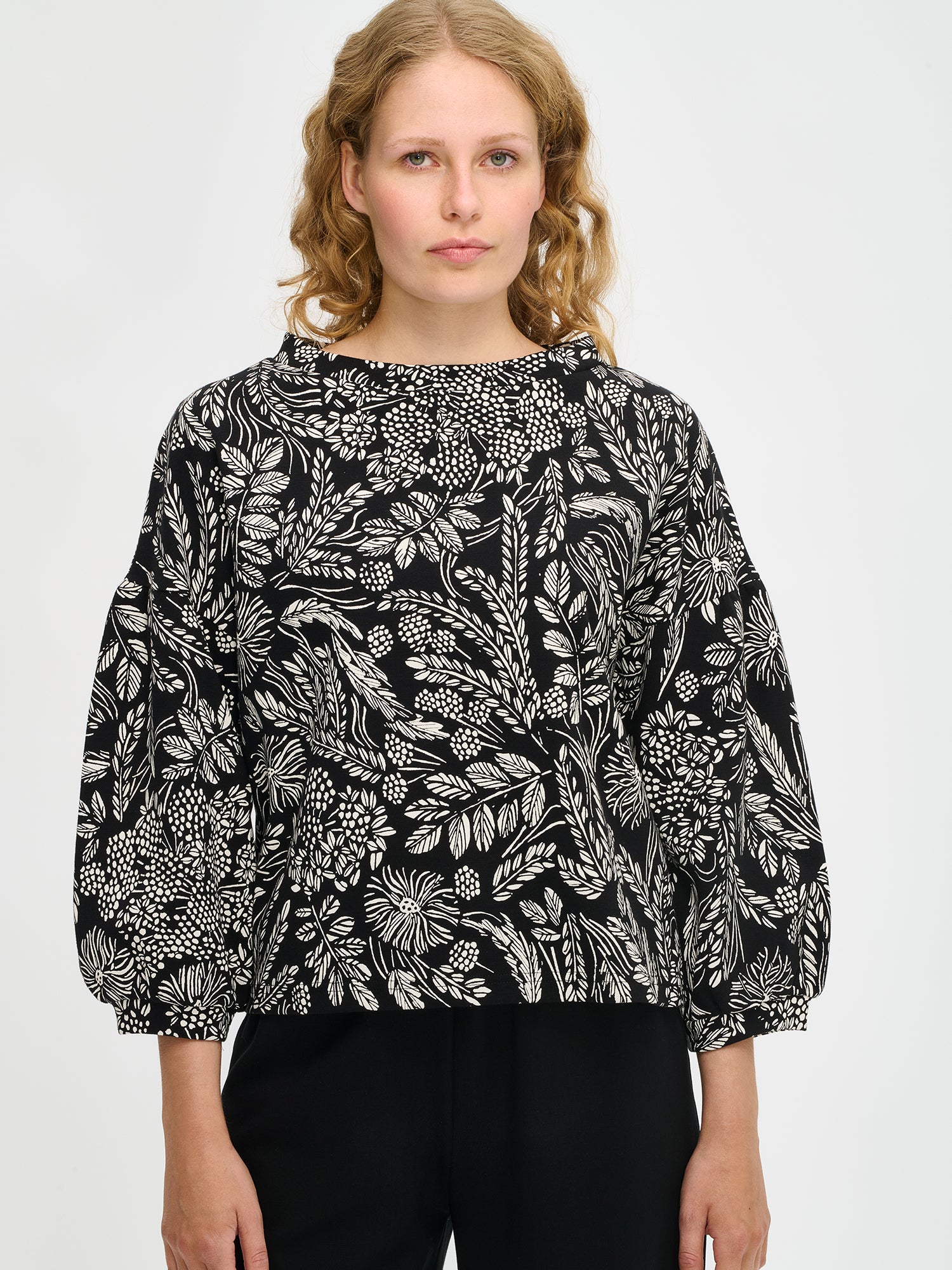 Nanson naisten mustavalkoinen Floora-pusero, kasviaiheinen kuosi ja poimuttuvat hihat, mallin yllä puolivartalokuvassa.