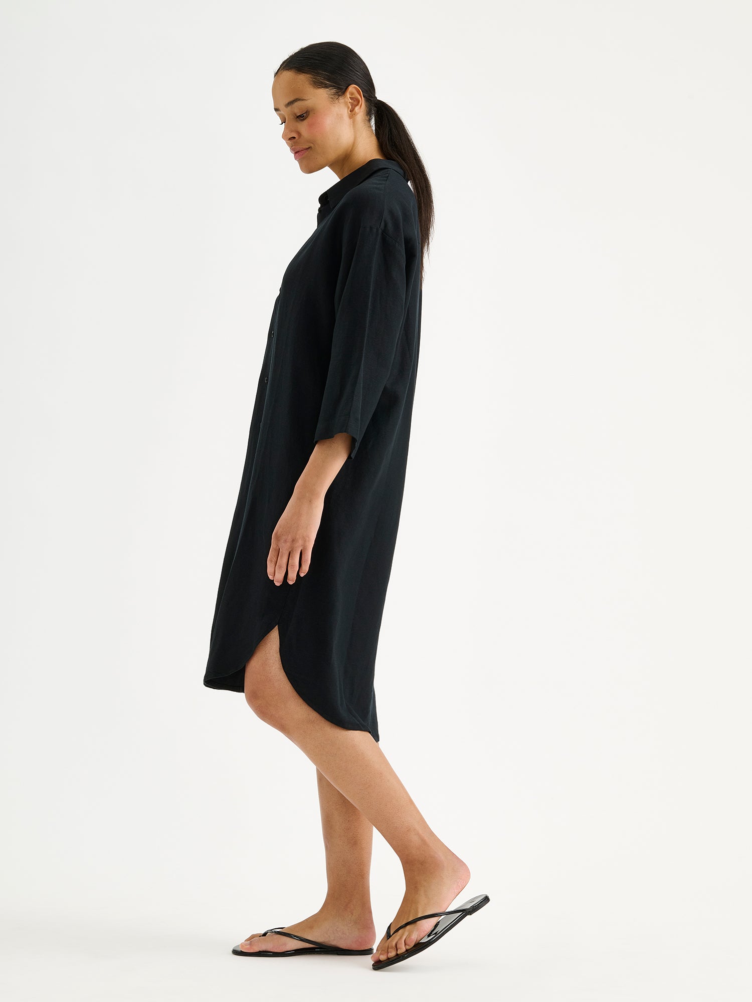 Nanson naisten musta ja mukavan rennon mallinen Irene-paitamekko mallin päällä sandaalien kanssa sivusta päin.