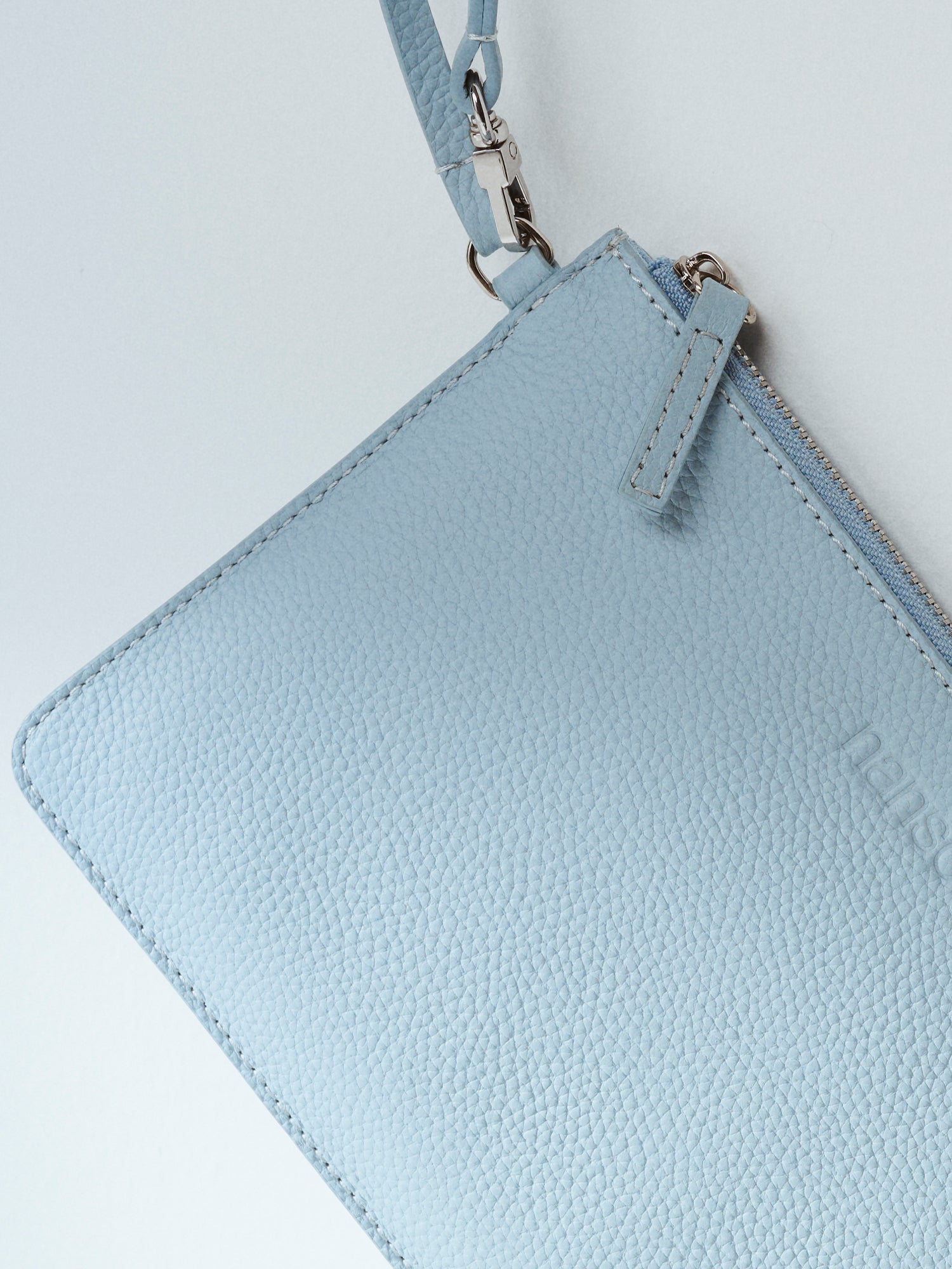 Nanson käytännöllinen ja tyylikäs vaaleansininen Naru Pieni- laukku toimii niin lompakkona kuin pikkulaukkuna. Nahkalaukussa on lyhyt kantohihna, jonka saa kiinnitettyä myös isomman laukun hihnaan. Laukun päällä on metallinen vetoketju. Nanson logo on painettu nahan pintaan laukun etu puolelle. Lähikuva materiaalista.