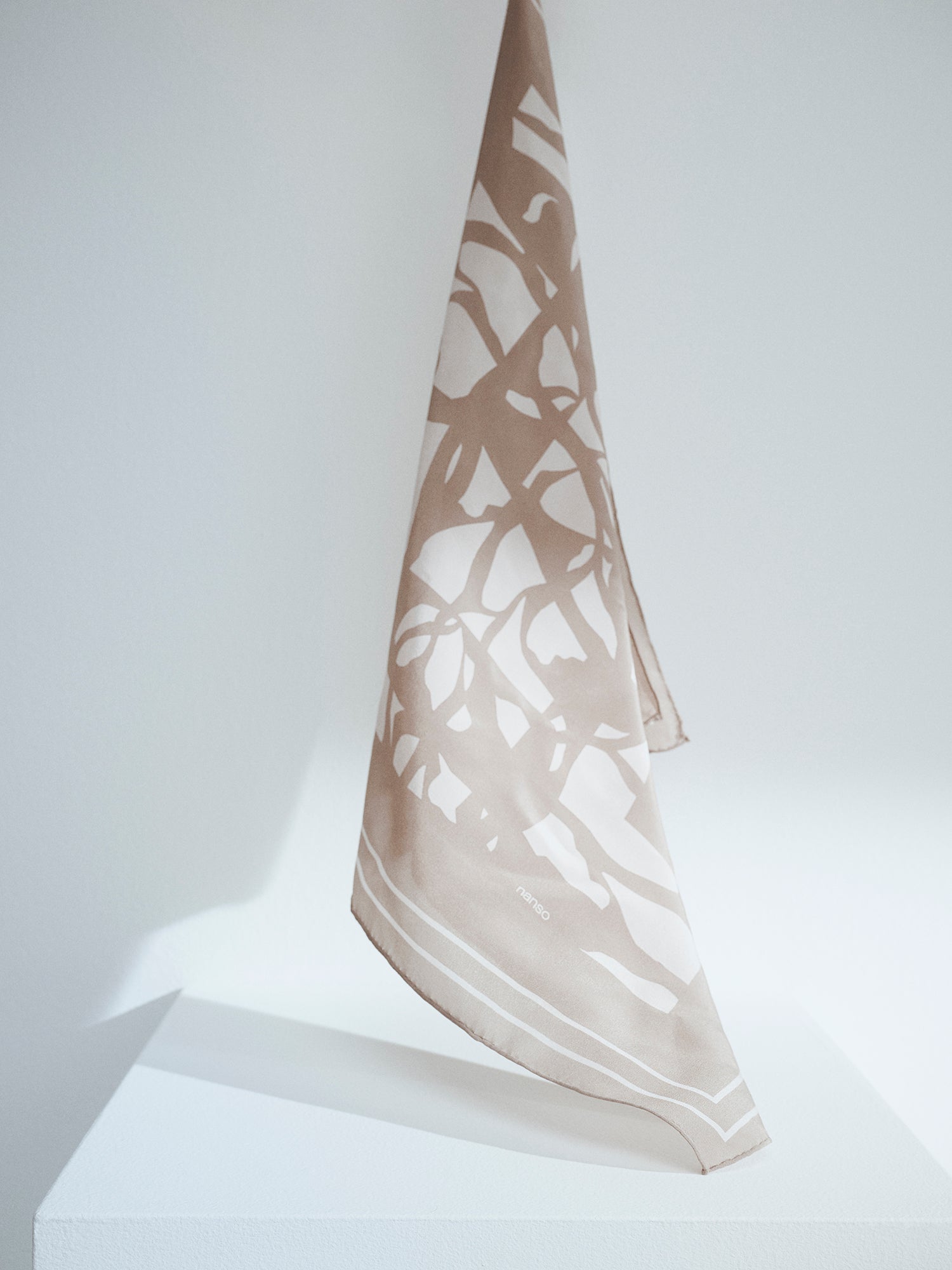 Naisten tyylikäs beige-valkoinen kuviollinen Palsta silkkihuivi tuotekuvassa roikkumassa auringonvalossa.