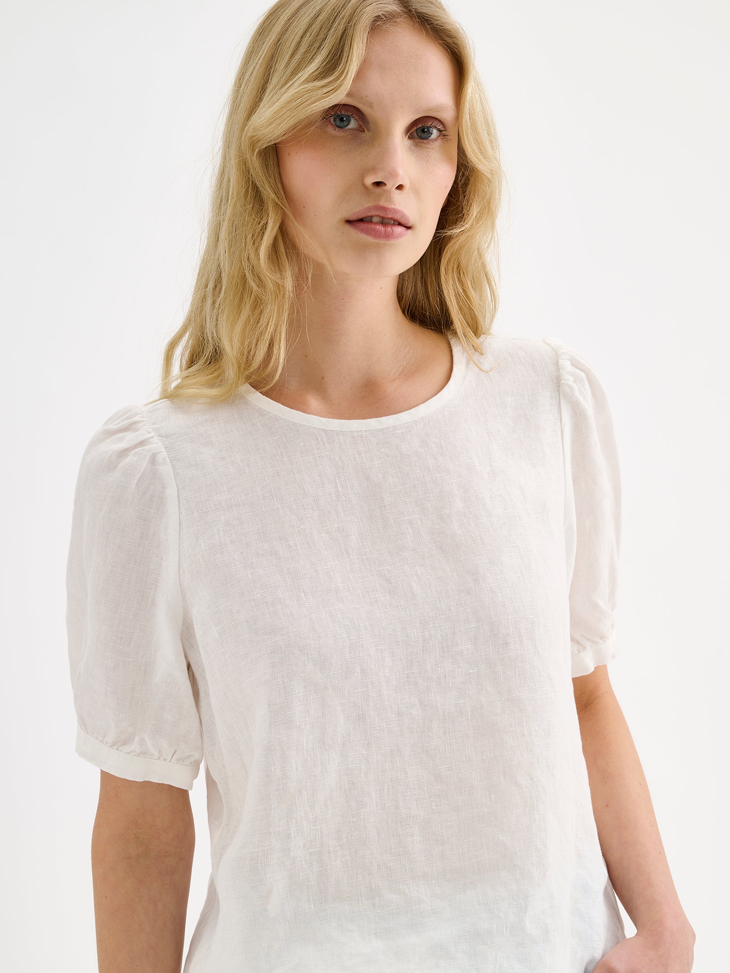 Nanson naisten kaunis valkoinen Sarastus-pellavapusero lyhyillä puhvihihoilla, mallin päällä lähikuvassa.