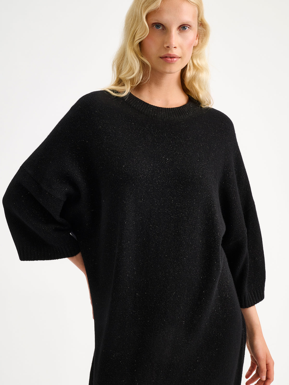 Nanson naisten rento, hieman oversized-mallinen musta kimaltava Lumine-neulemekko mallin päällä pitsisukkahousujen kanssa.