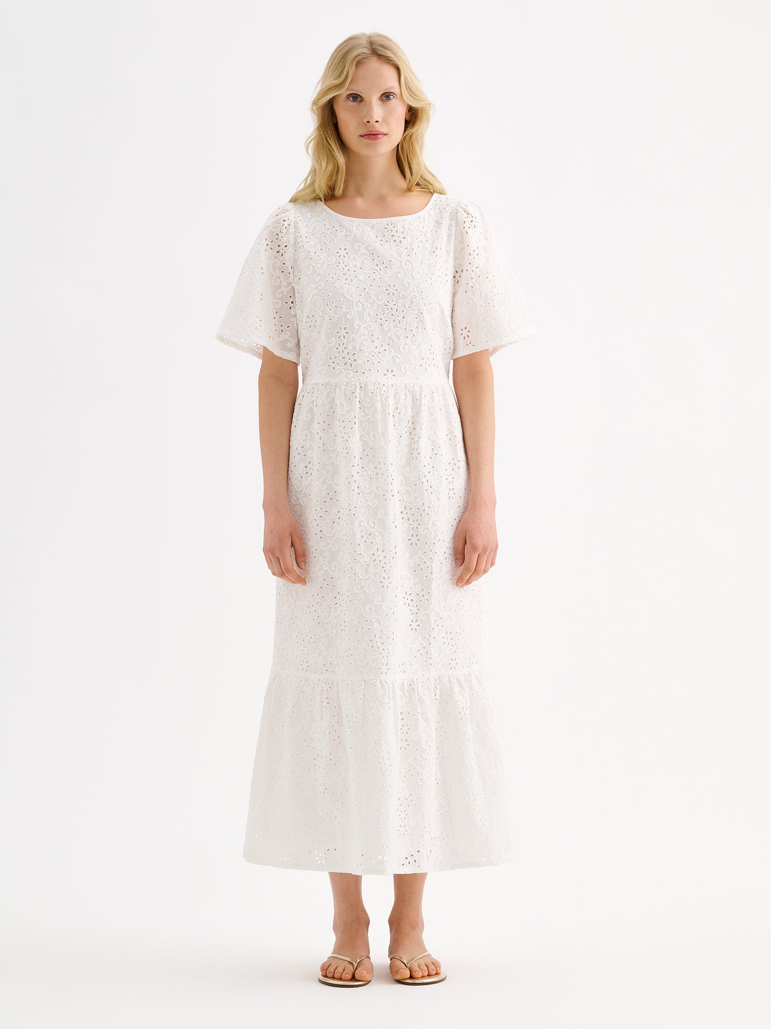 Nanson naisten kaunis pitkä luonnonvalkoinen Odette-mekko pitsimäisestä Broderie anglaise -tyyppisestä puuvillakankaasta mallin päällä sandaalien kanssa.