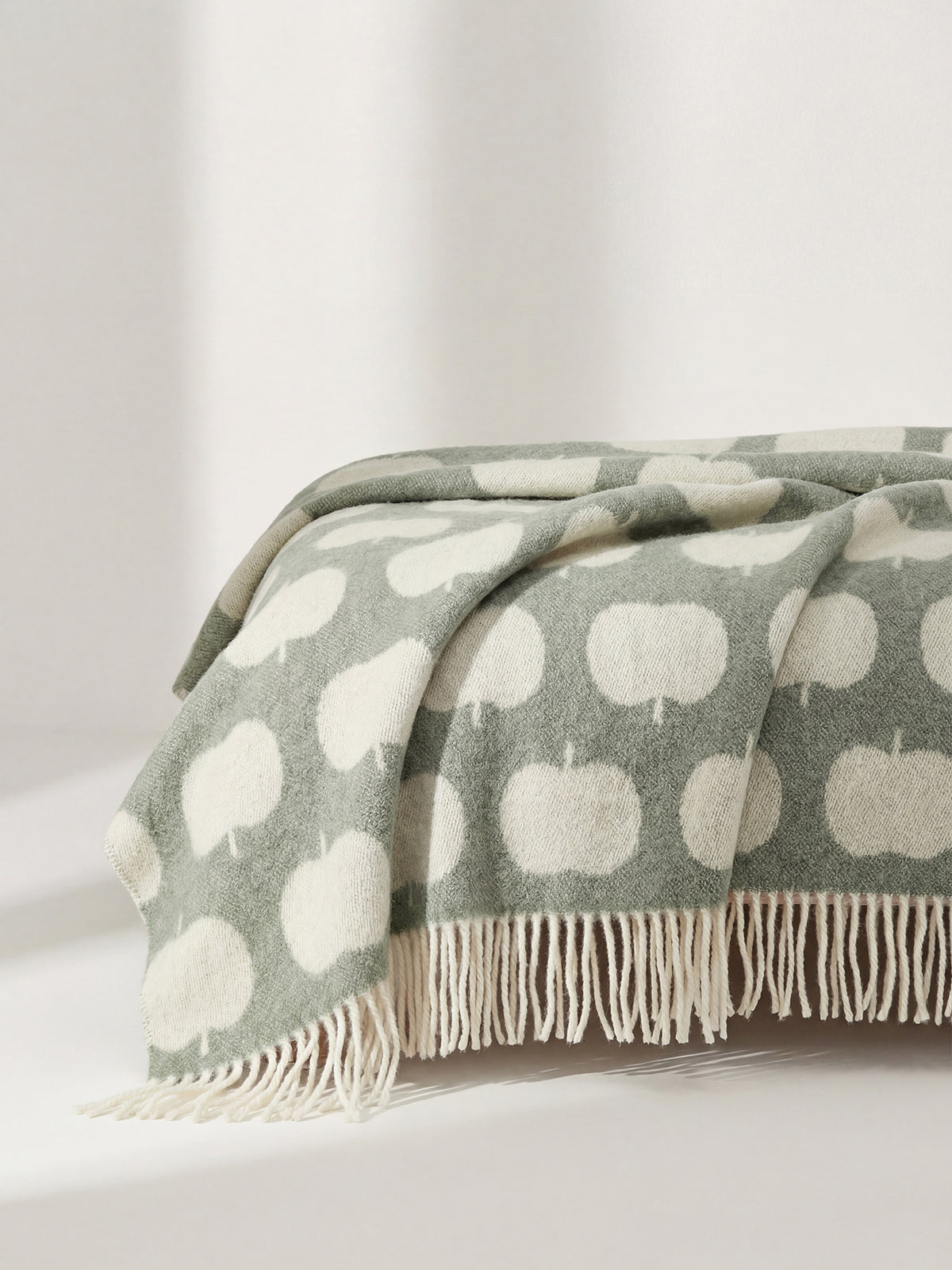 Nanson villainen vihreän sävyinen Omppu-villahuopa, jonka lyhyitä sivuja koristaa kierrehapsut. Villahuopa on kudottu jacquard-tekniikalla. Kuvattuna rahin päällä.