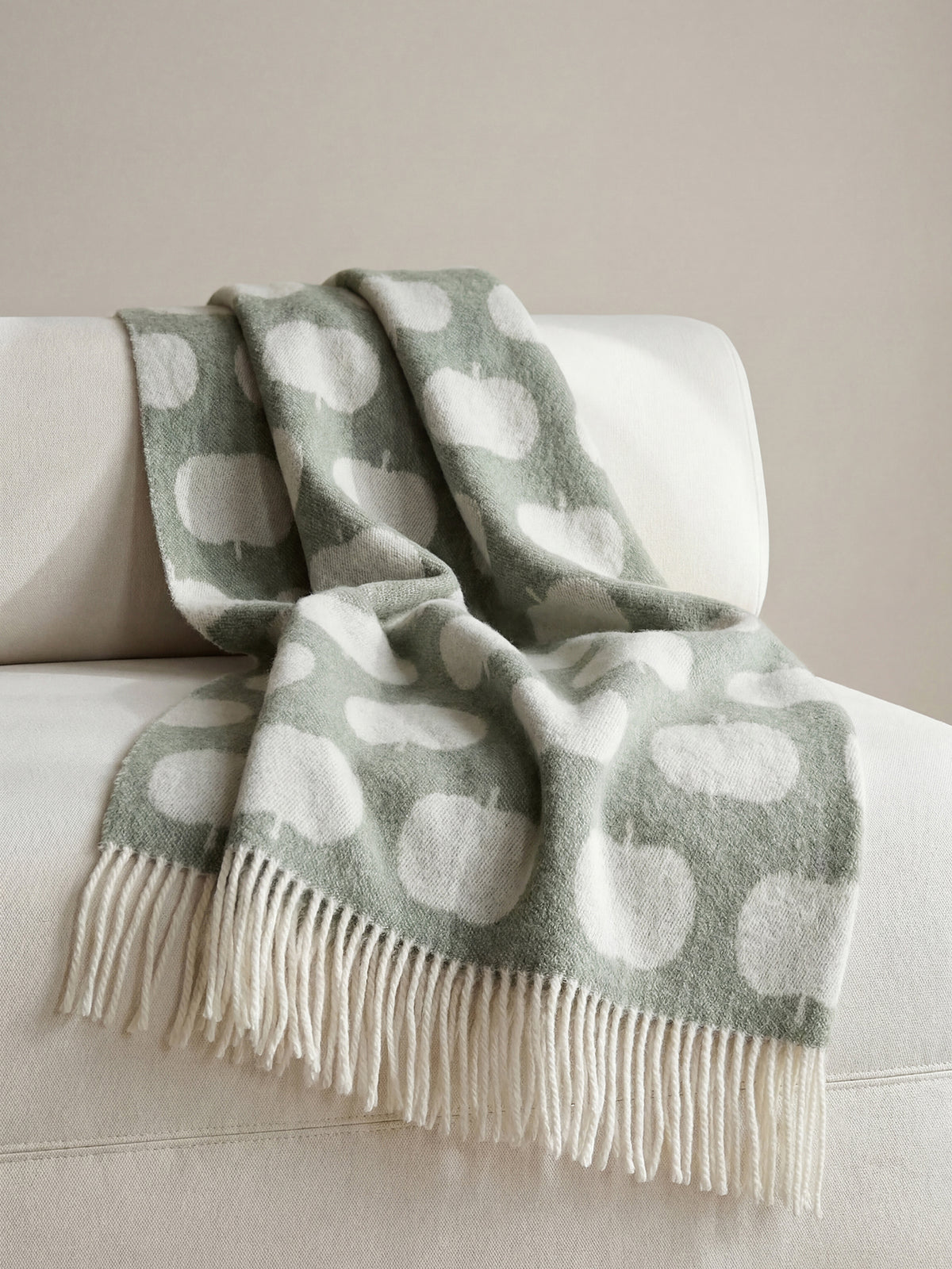 Nanson villainen vihreän sävyinen Omppu-villahuopa, jonka lyhyitä sivuja koristaa kierrehapsut. Villahuopa on kudottu jacquard-tekniikalla. Kuvattuna nojatuolin päällä. 