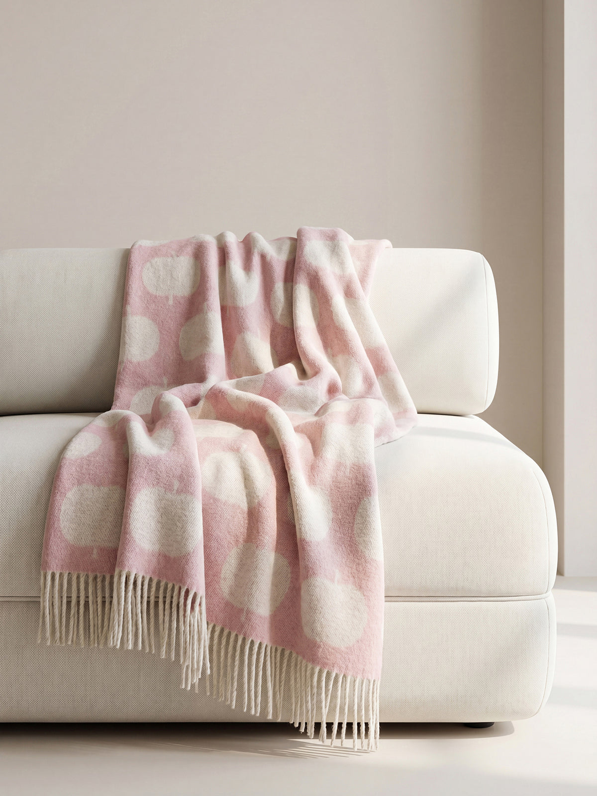 Nanson villainen roosan sävyinen Omppu-villahuopa, jonka lyhyitä sivuja koristaa kierrehapsut. Villahuopa on kudottu jacquard-tekniikalla. Kuvassa aseteltuna nojatuolille.