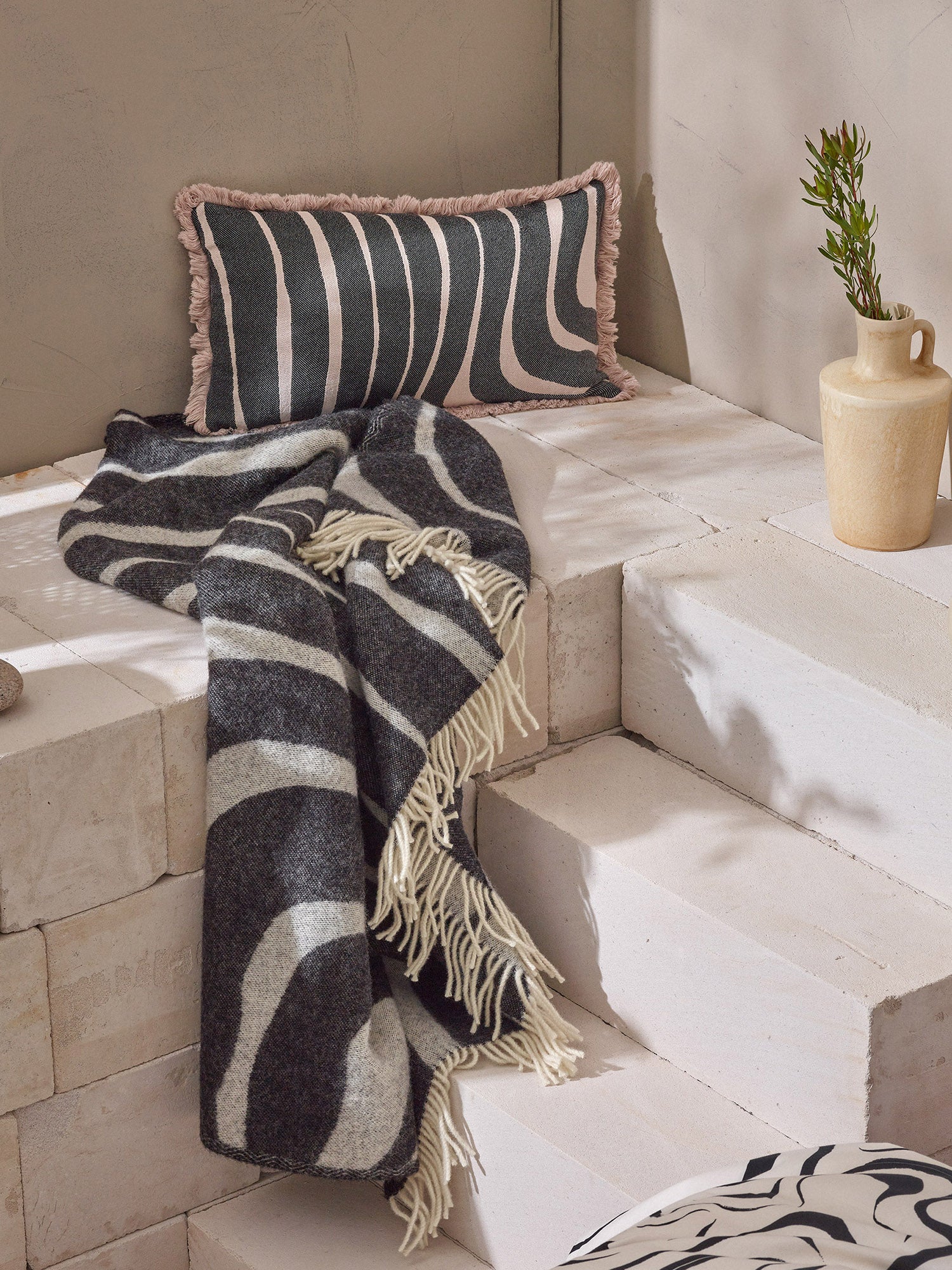 Kuvassa sisustussetin tuotteet: huopa ja sisustustyynynpäällinen kauniissa asetelmassa.